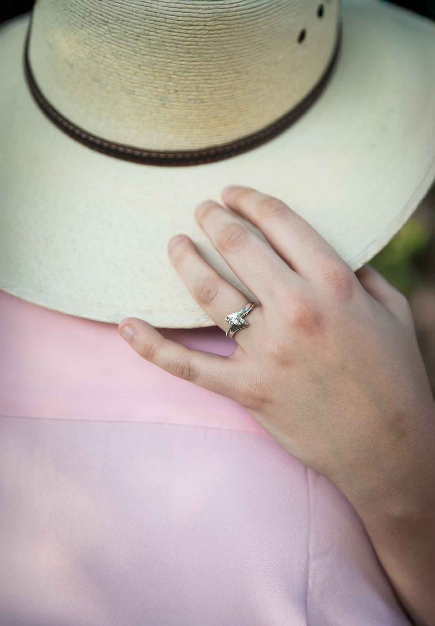 Close up of woman's hand showing engagement ring touching man on back wearing cowboy hat and pink shirt
