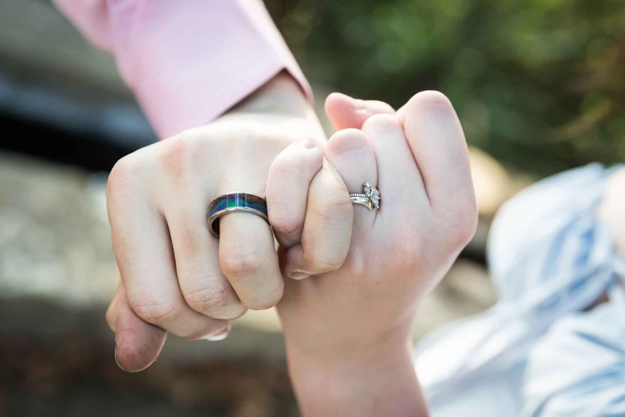 Close up of a man and woman interlocking hands at the pinky fingers showing engagemenet rings