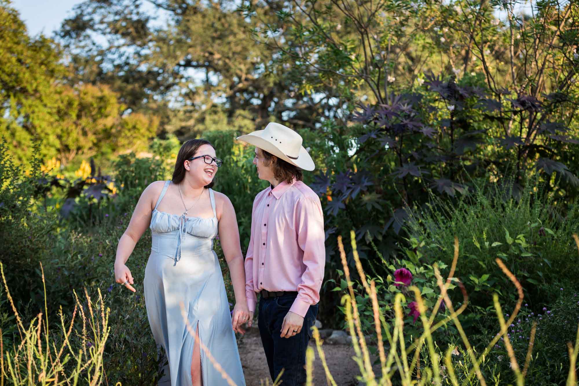 San Antonio Botanical Garden engagement photos of woman and man wearing cowboy hat walking down garden pathway
