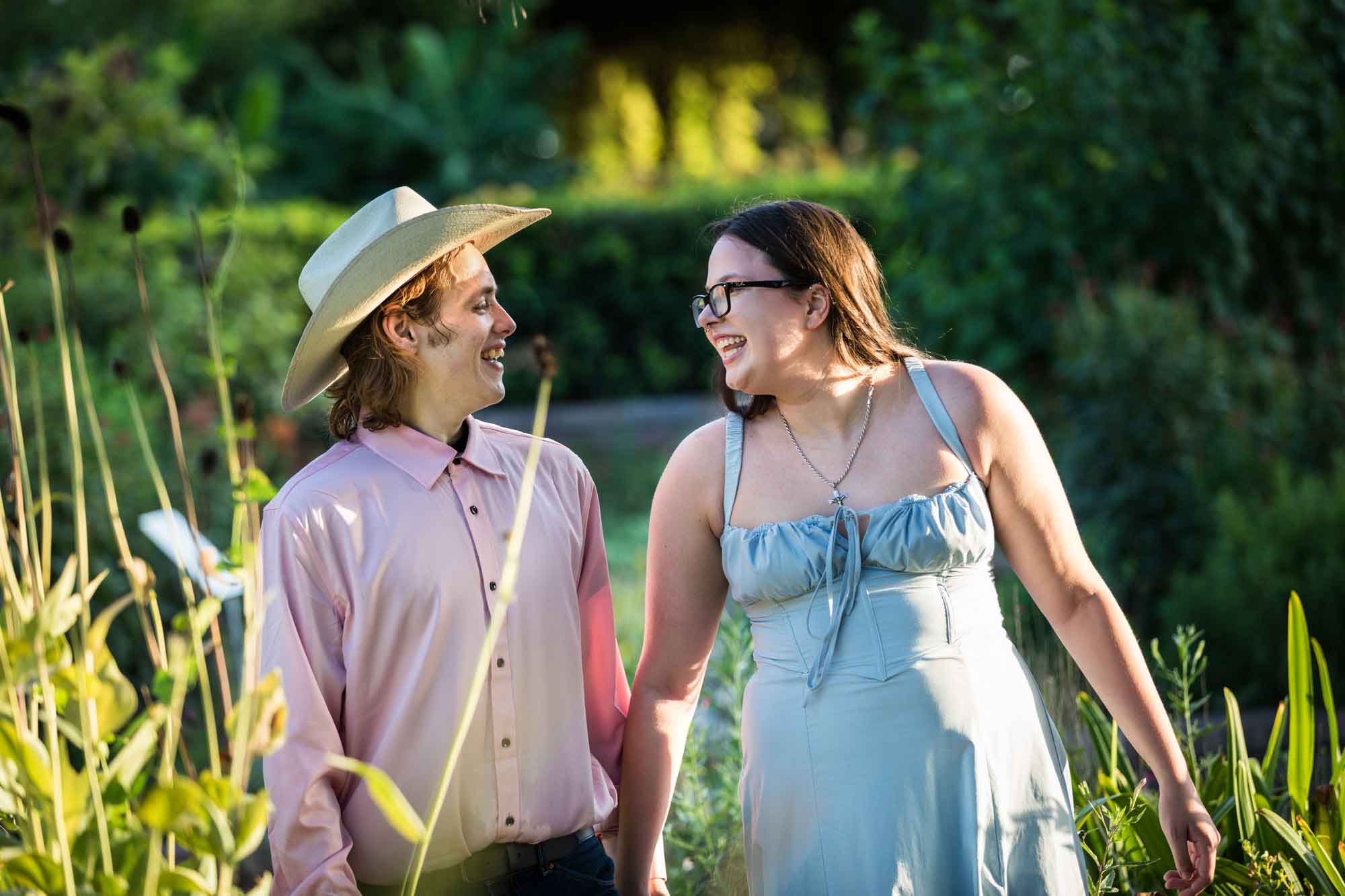 San Antonio Botanical Garden engagement photos of woman and man wearing cowboy hat walking down garden pathway