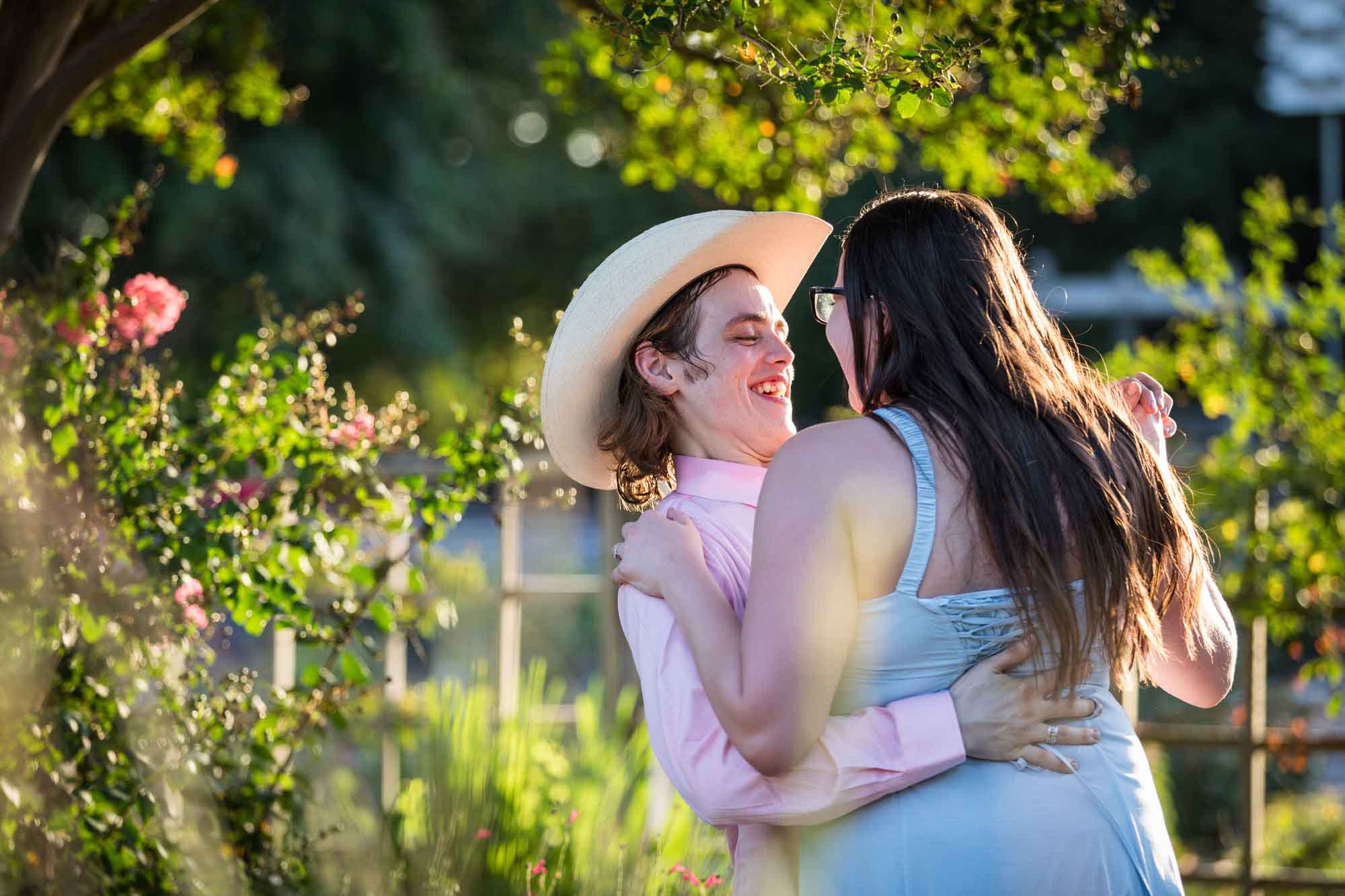 San Antonio Botanical Garden engagement photos of woman and man wearing cowboy hat dancing in garden pathway at sunset