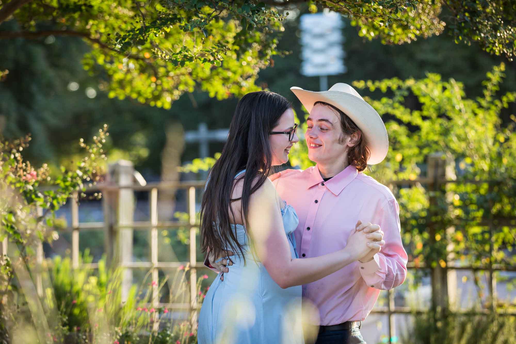San Antonio Botanical Garden engagement photos of woman and man wearing cowboy hat dancing in garden pathway at sunset