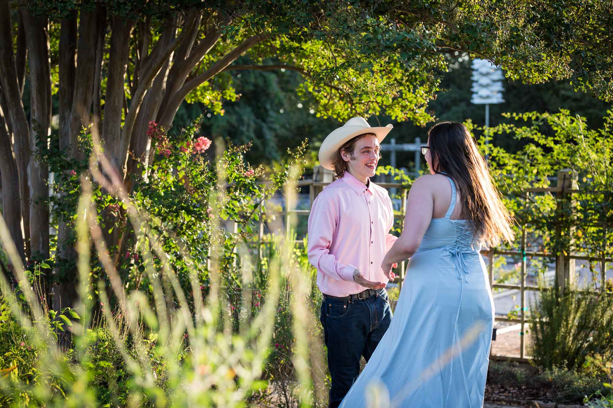 San Antonio Botanical Garden engagement photos of woman and man wearing cowboy hat dancing in garden pathway at sunset
