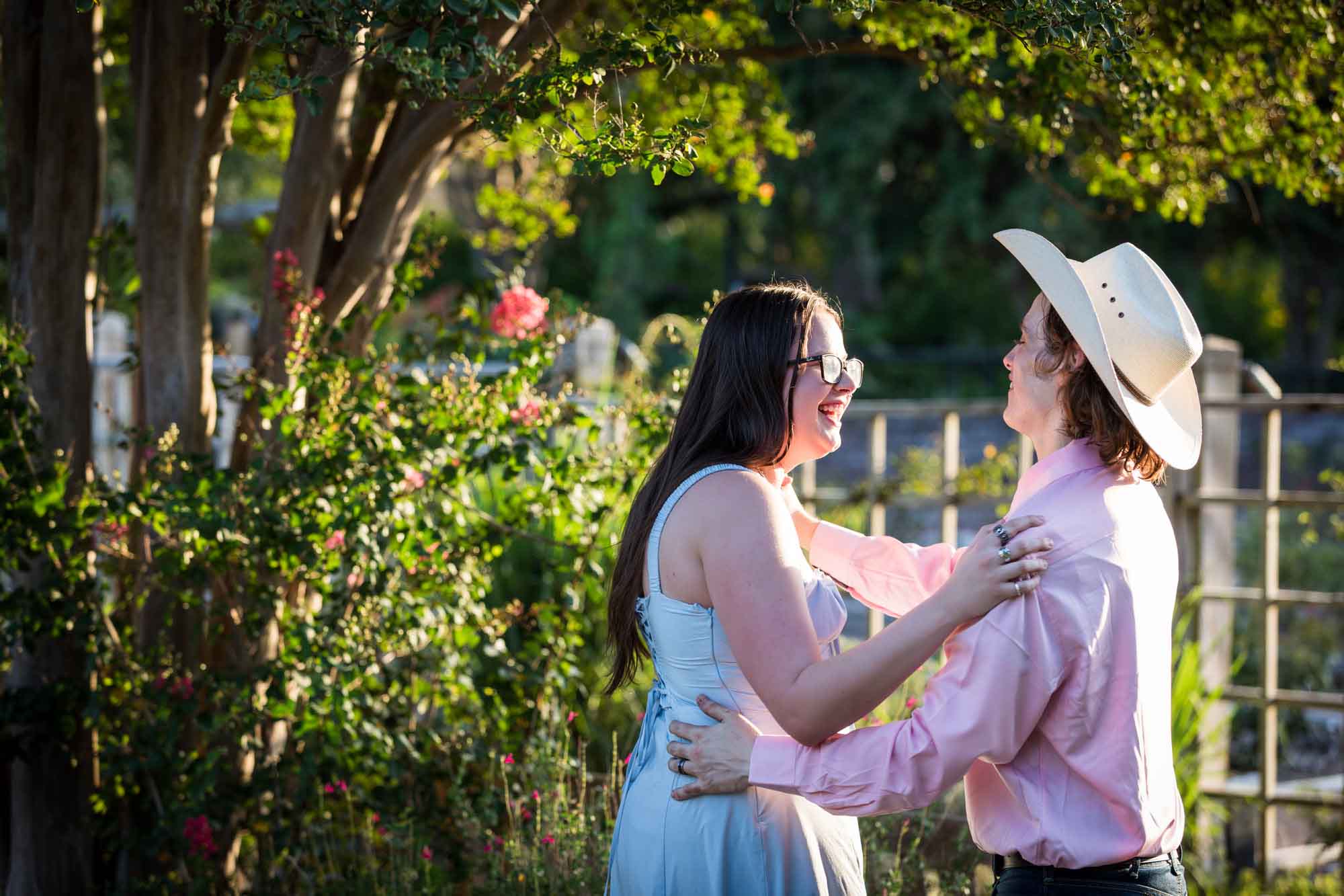 San Antonio Botanical Garden engagement photos of woman and man wearing cowboy hat dancing in garden pathway at sunset