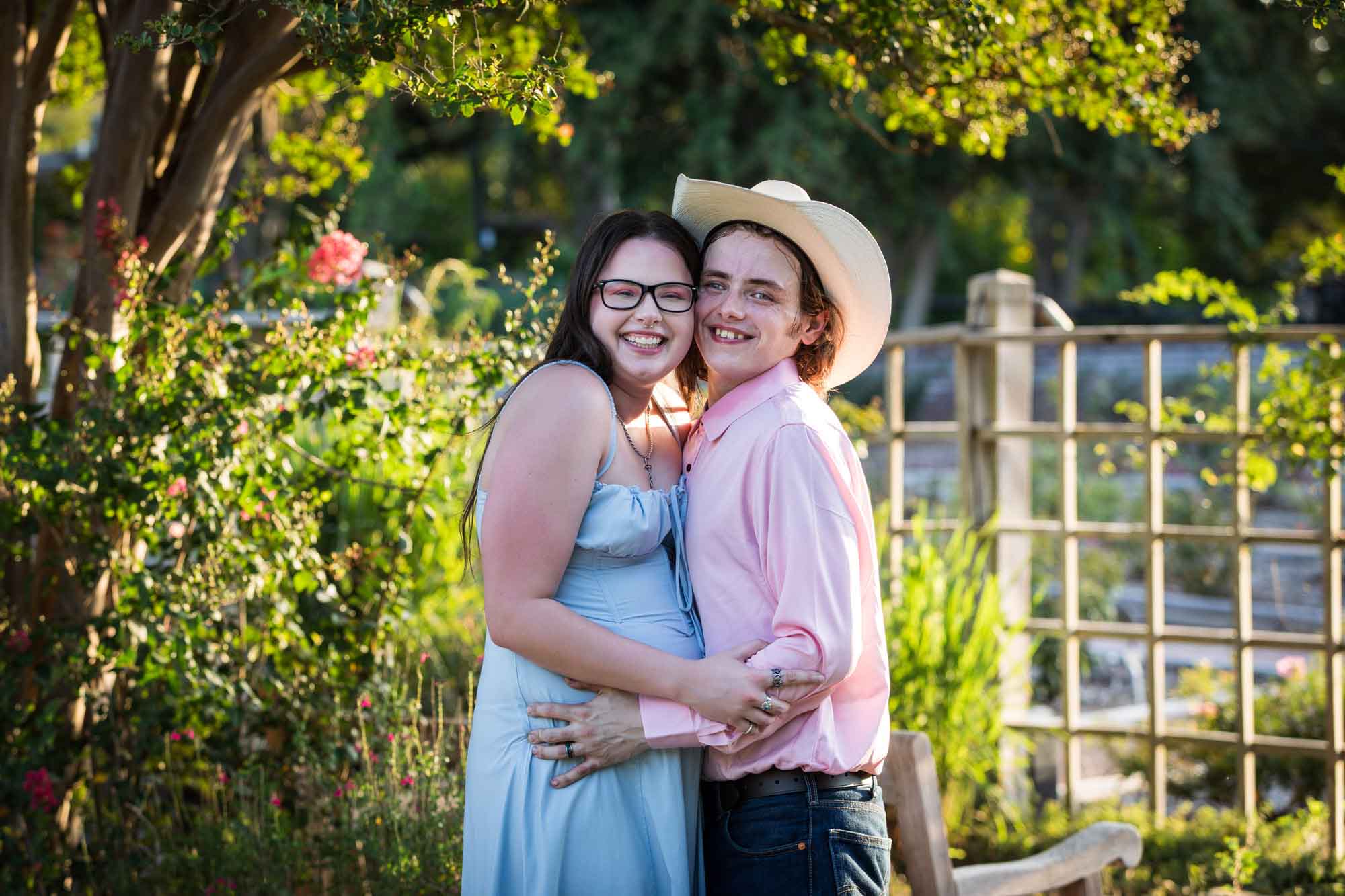 San Antonio Botanical Garden engagement photos of woman and man wearing cowboy hat hugging in garden pathway at sunset