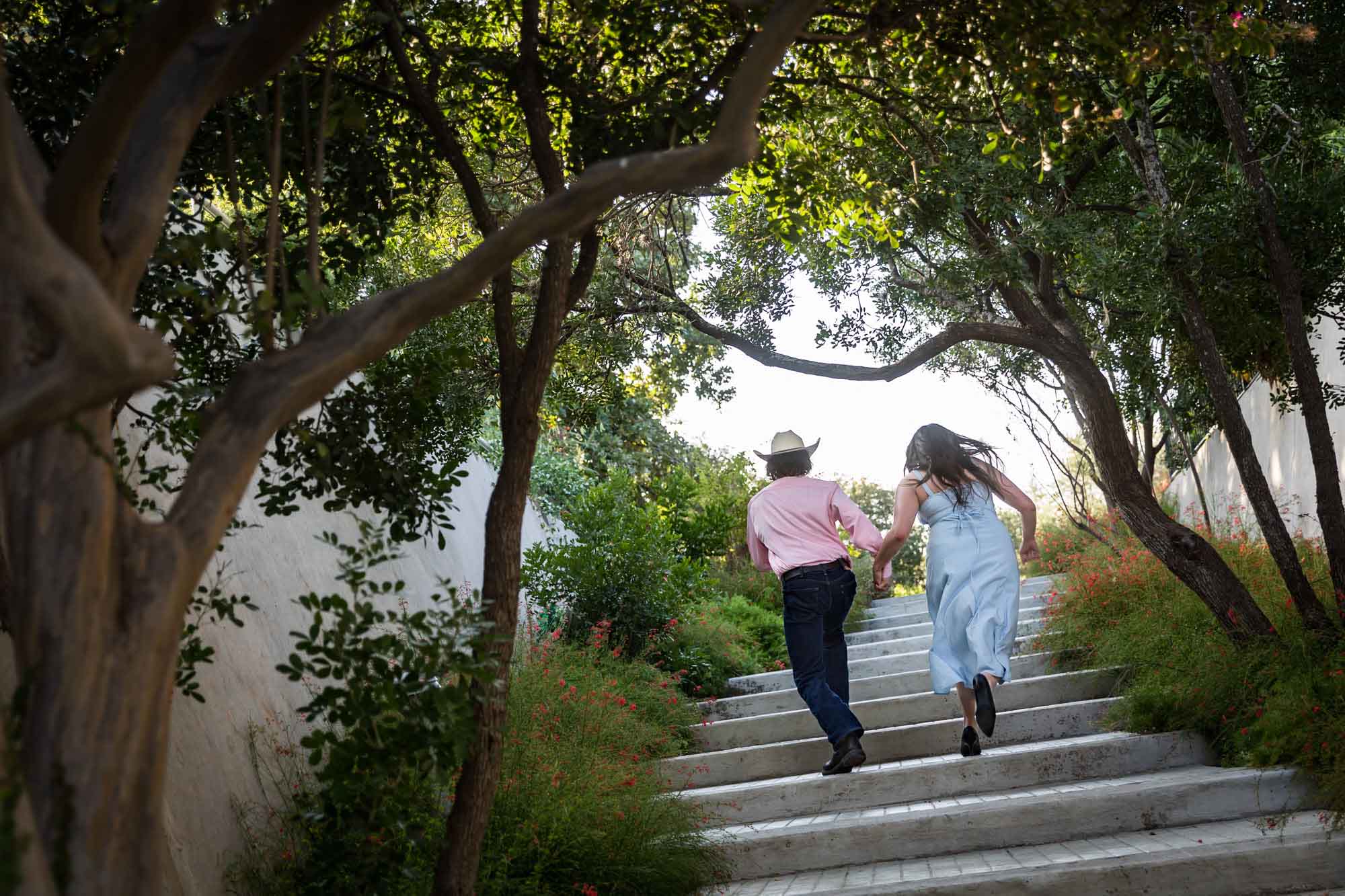 San Antonio Botanical Garden engagement photos of couple running to the top of staircase