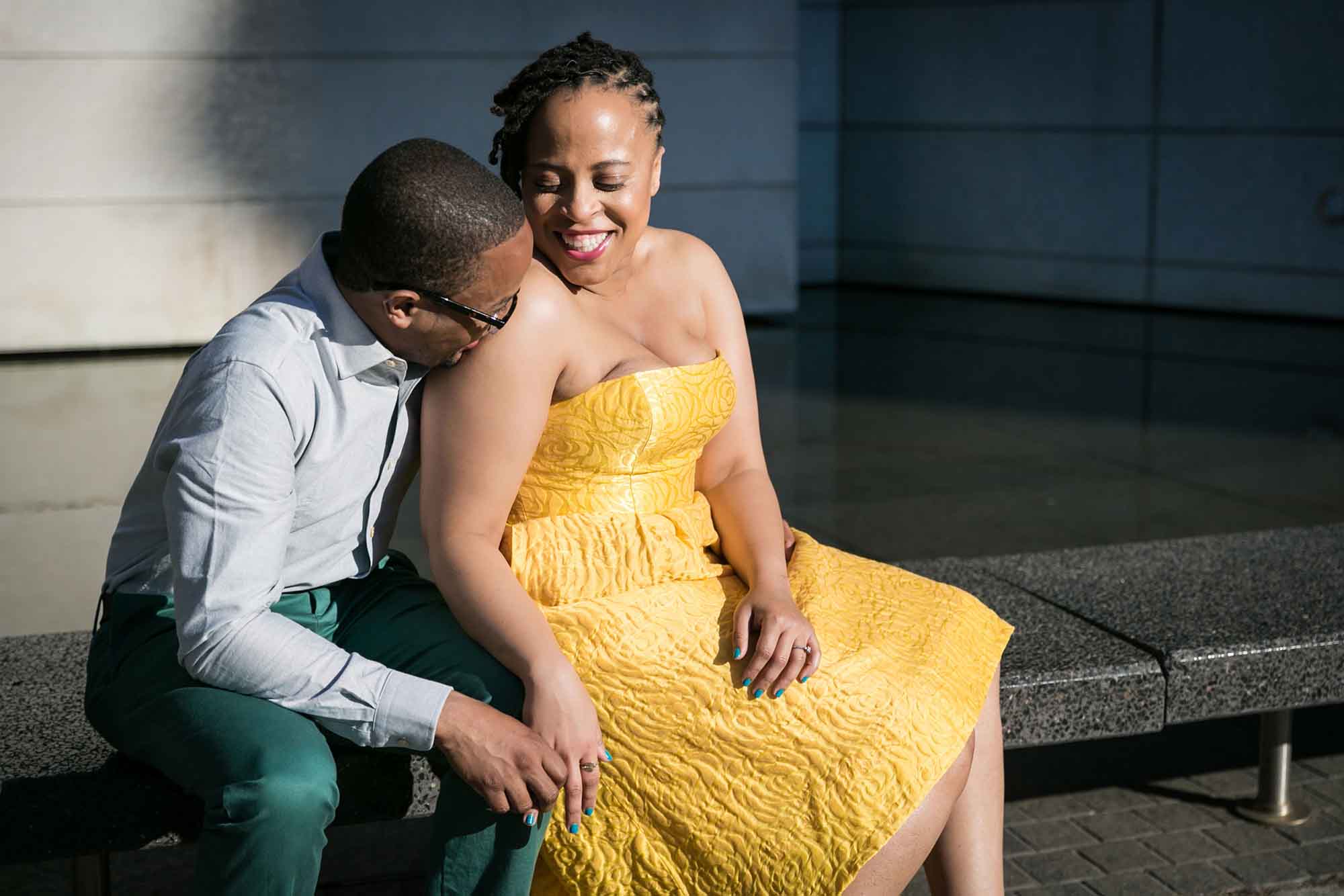 African American woman wearing strapless yellow dress sitting beside African American man wearing white shirt and green pants during engagement session