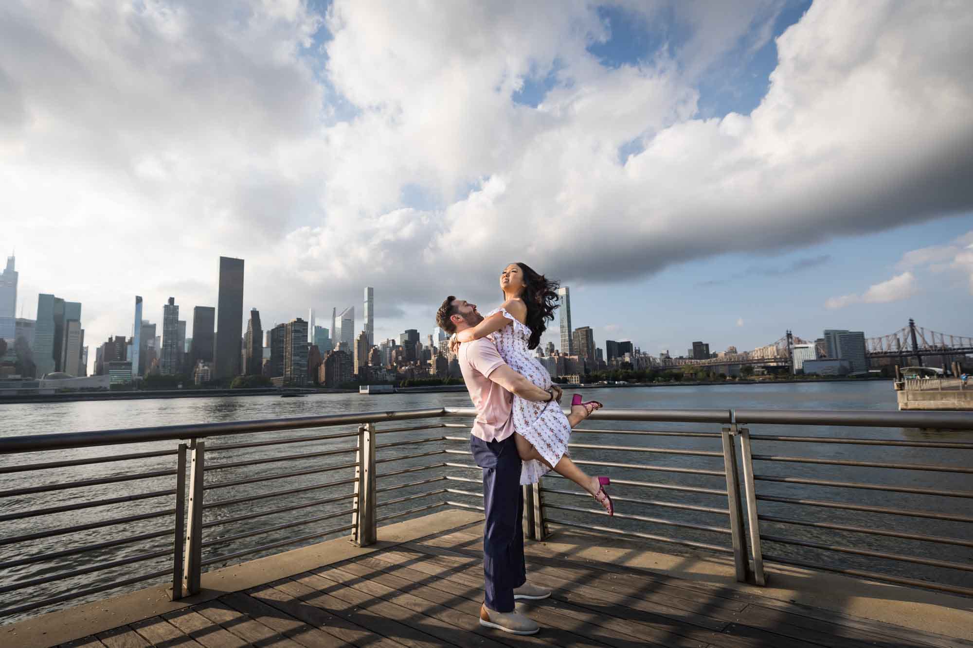 Man lifting woman in the air at Gantry Plaza State Park during an engagement photo shoot