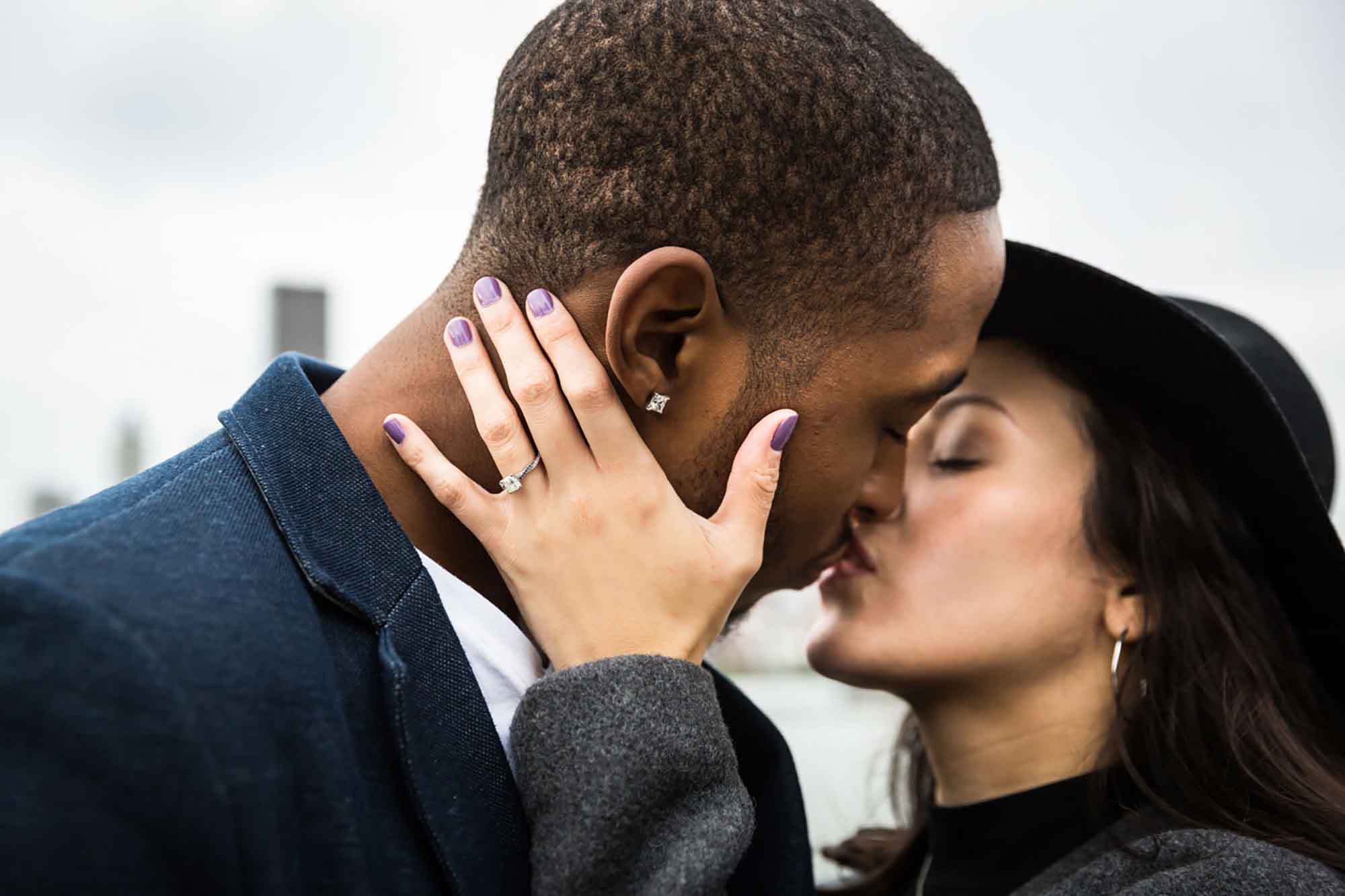 Close up of white woman with hand showing engagement ring kissing African American man during engagement photo shoot