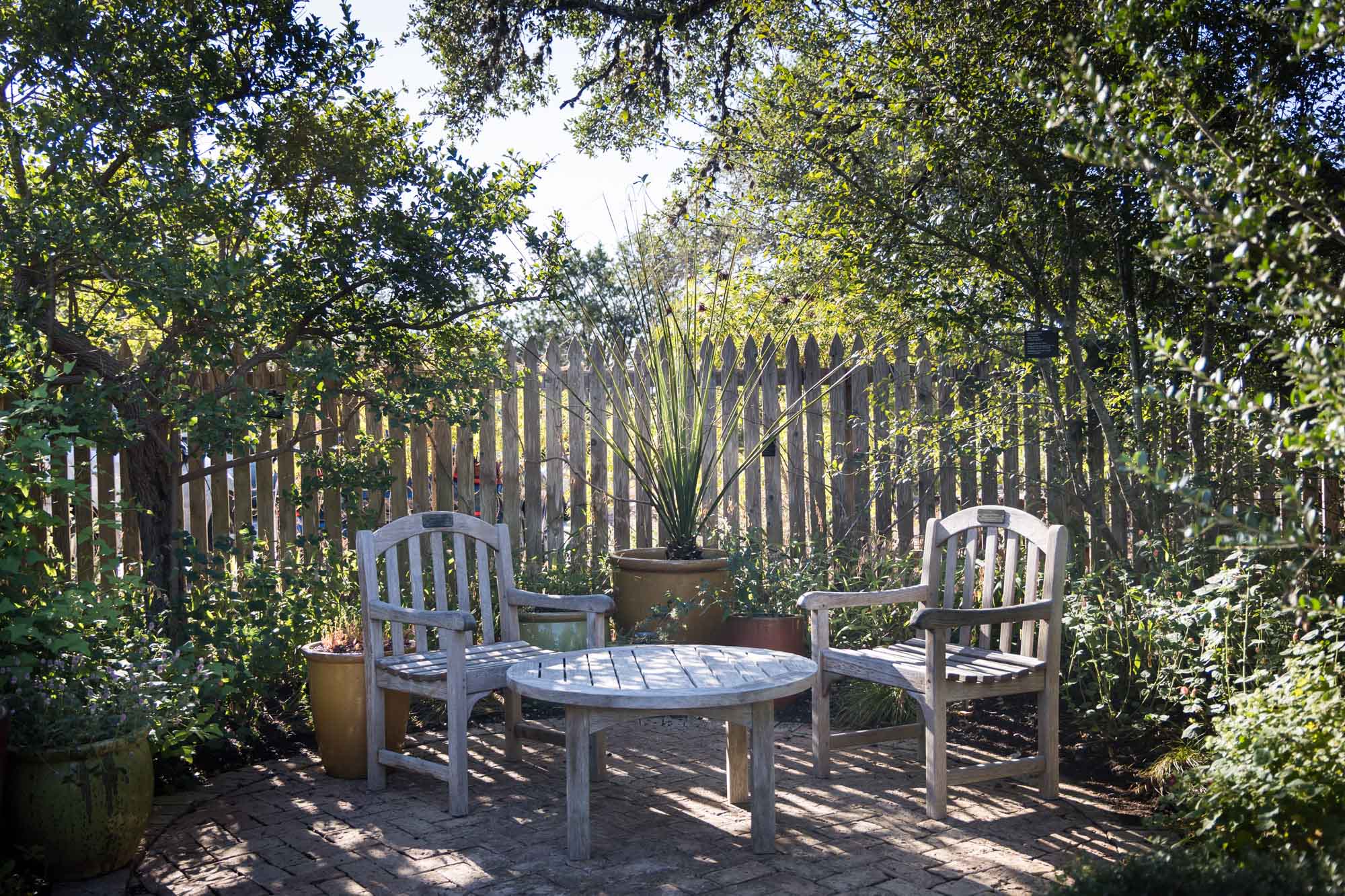 Two wooden chairs and table in front of wooden fence at the Lady Bird Johnson Wildflower Center for an article on the best places to propose in Austin