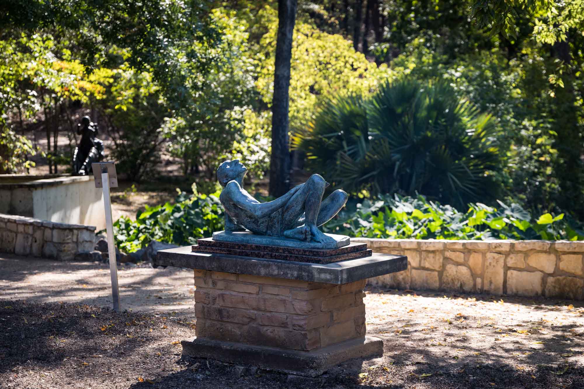 Reclining sculpture on a stone platform in front of plant beds at the Umlauf Sculpture Garden for an article on the best places to propose in Austin