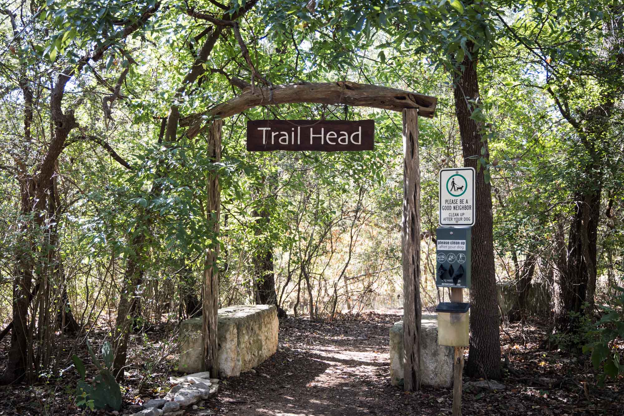 Wooden sign that says 'Trail Head' with dog pet waste bags to on post to the right in a forest for an article on Cibolo Nature Center surprise proposal tips