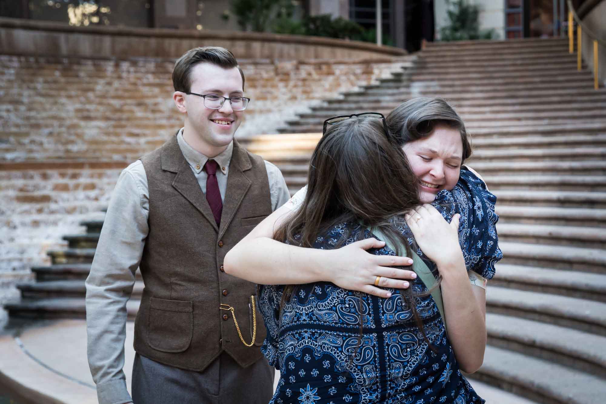 Two women hugging in front of man at Weston Centre during a River Walk surprise proposal