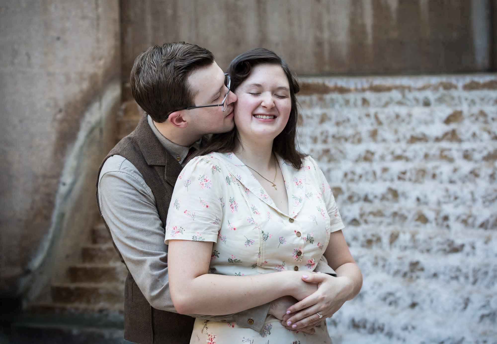 Man kissing woman on cheek in front of waterfall and stairs at Weston Centre during a River Walk surprise proposal