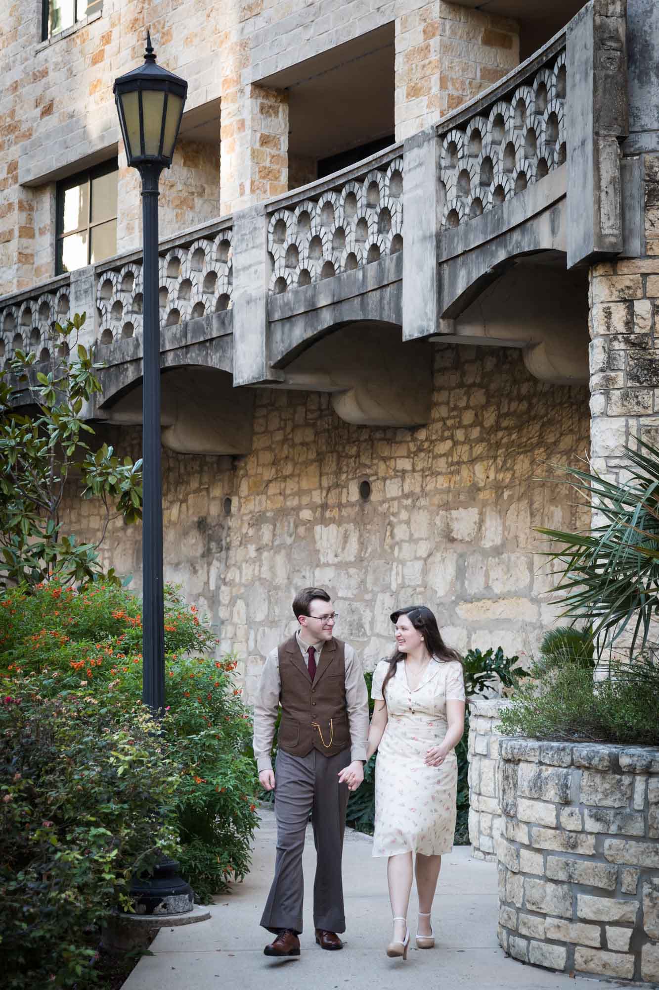 Couple walking down pathway in front of lamp post and green bushes during a River Walk surprise proposal