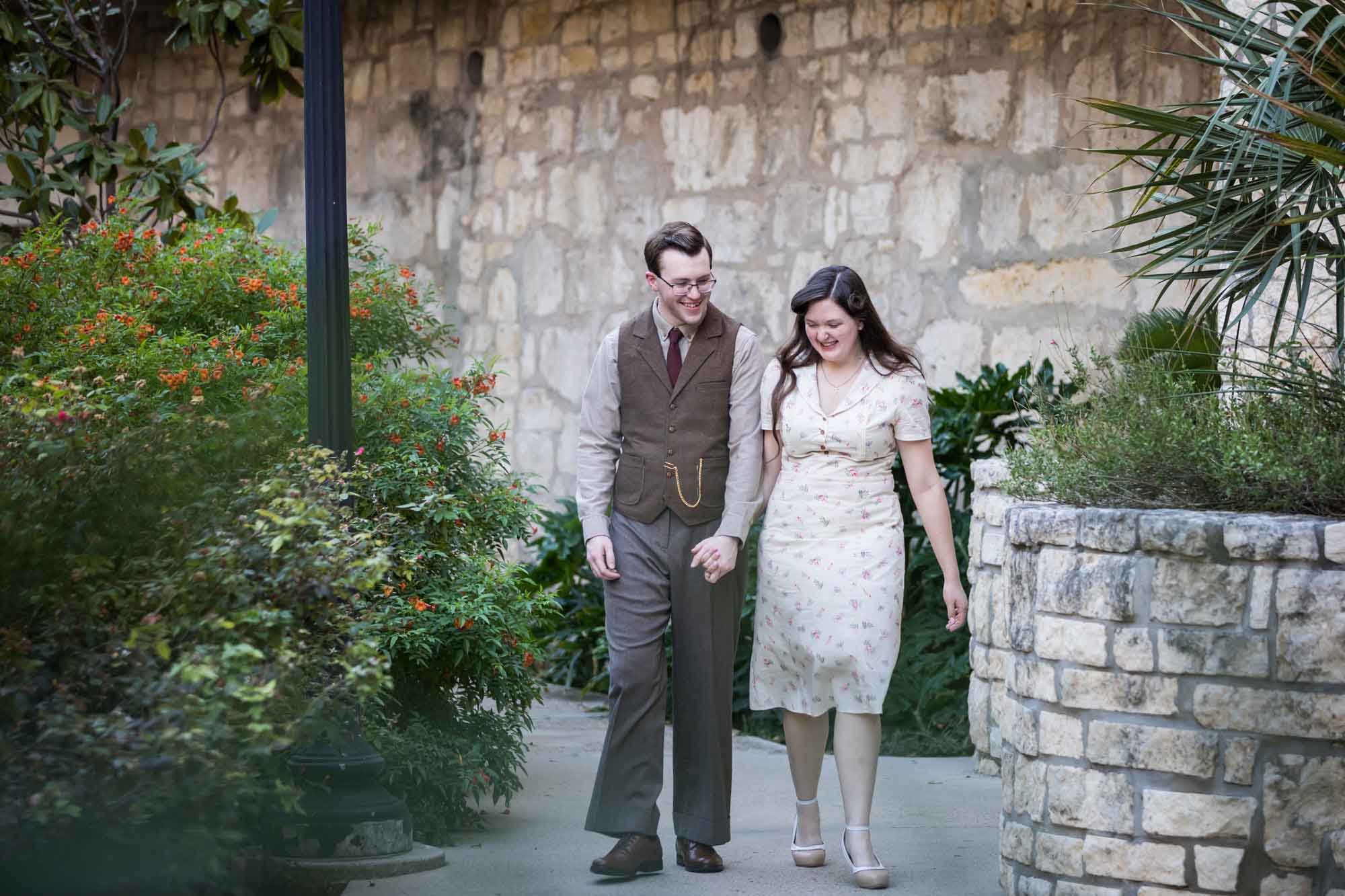 Couple walking down pathway in front of lamp post and green bushes during a River Walk surprise proposal