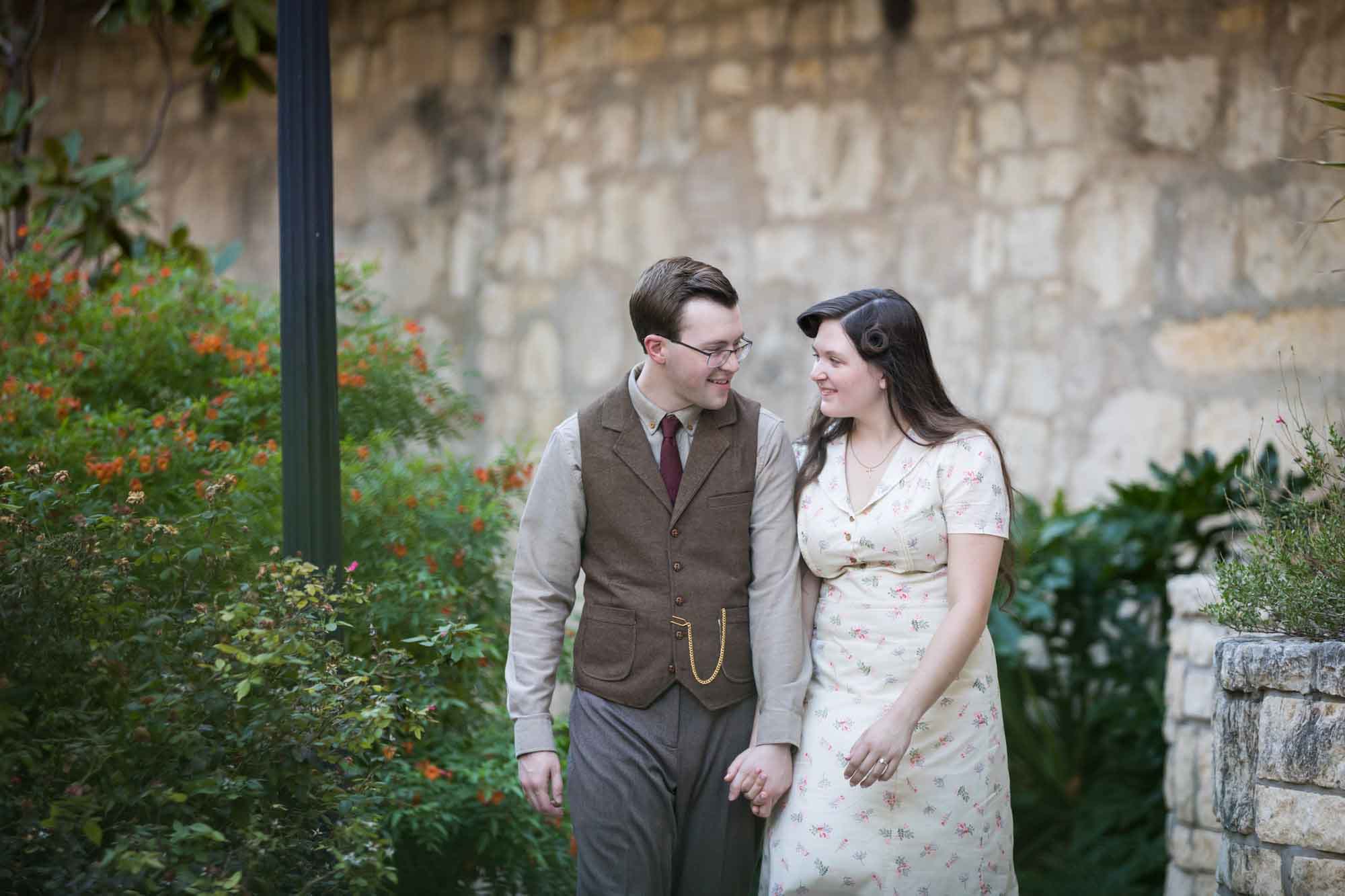 Couple walking down pathway in front of lamp post and green bushes during a River Walk surprise proposal