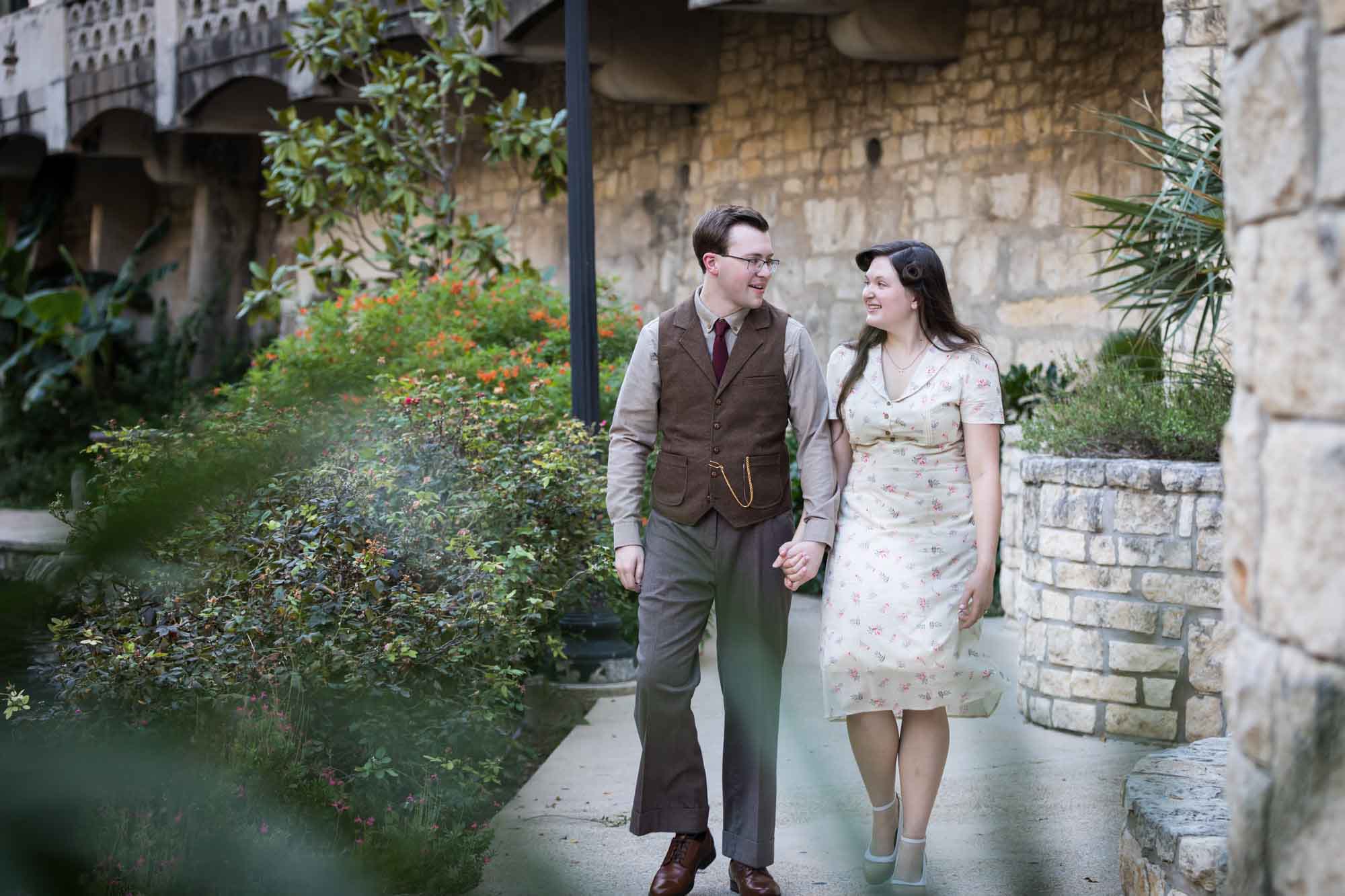 Couple walking down pathway in front of lamp post and green bushes during a River Walk surprise proposal