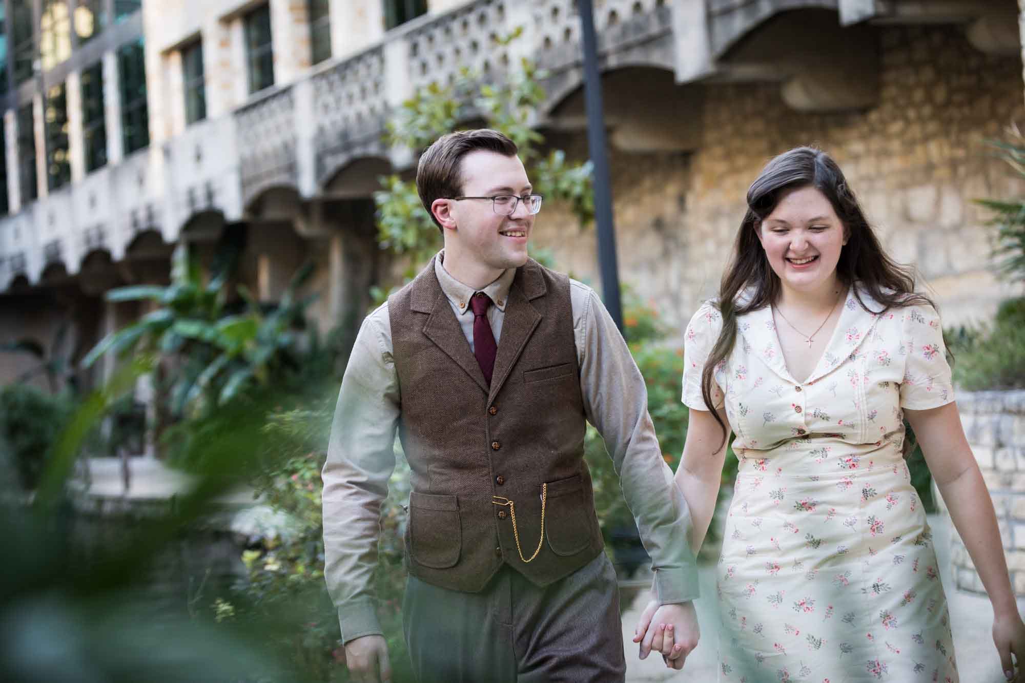 Couple walking down pathway in front of lamp post and green bushes during a River Walk surprise proposal