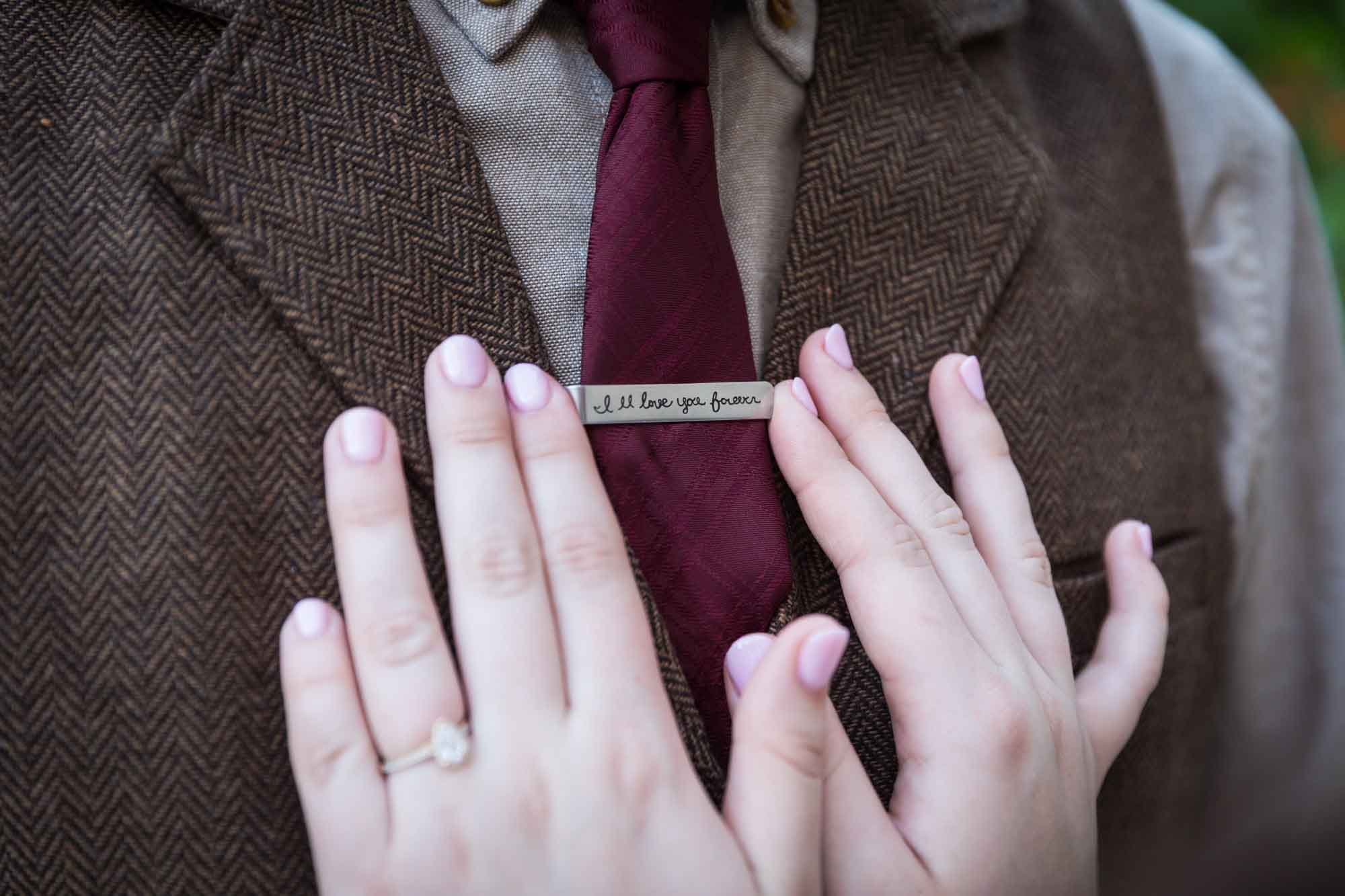 Close up of woman's hands on man's tie clip which says 'I'll Love You Forever'