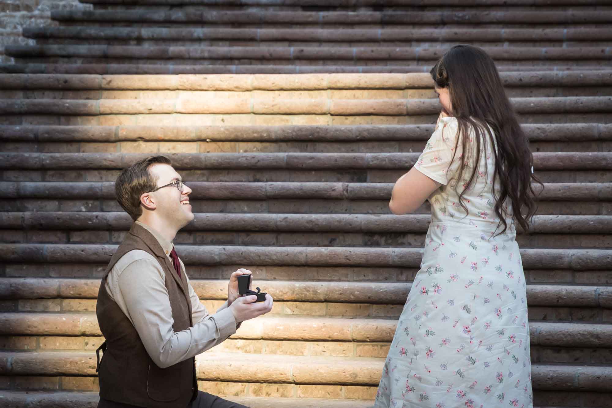 Man down on bended knee proposing to girlfriend on the Weston Centre stairs during a River Walk surprise proposal
