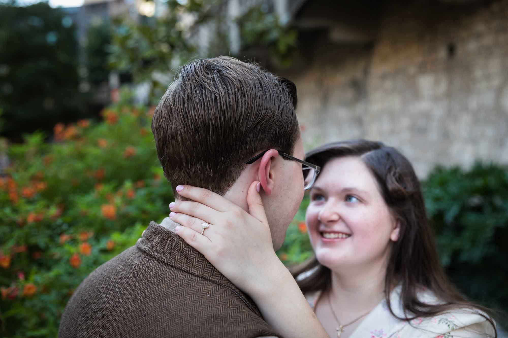 Couple looking at each other with woman's hand showing engagement ring around man's neck during a River Walk surprise proposal