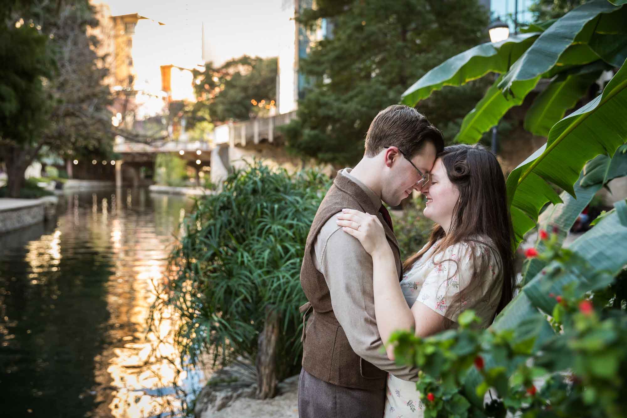 Couple hugging each other and pressing foreheads against each other surrounded by plants during a River Walk surprise proposal