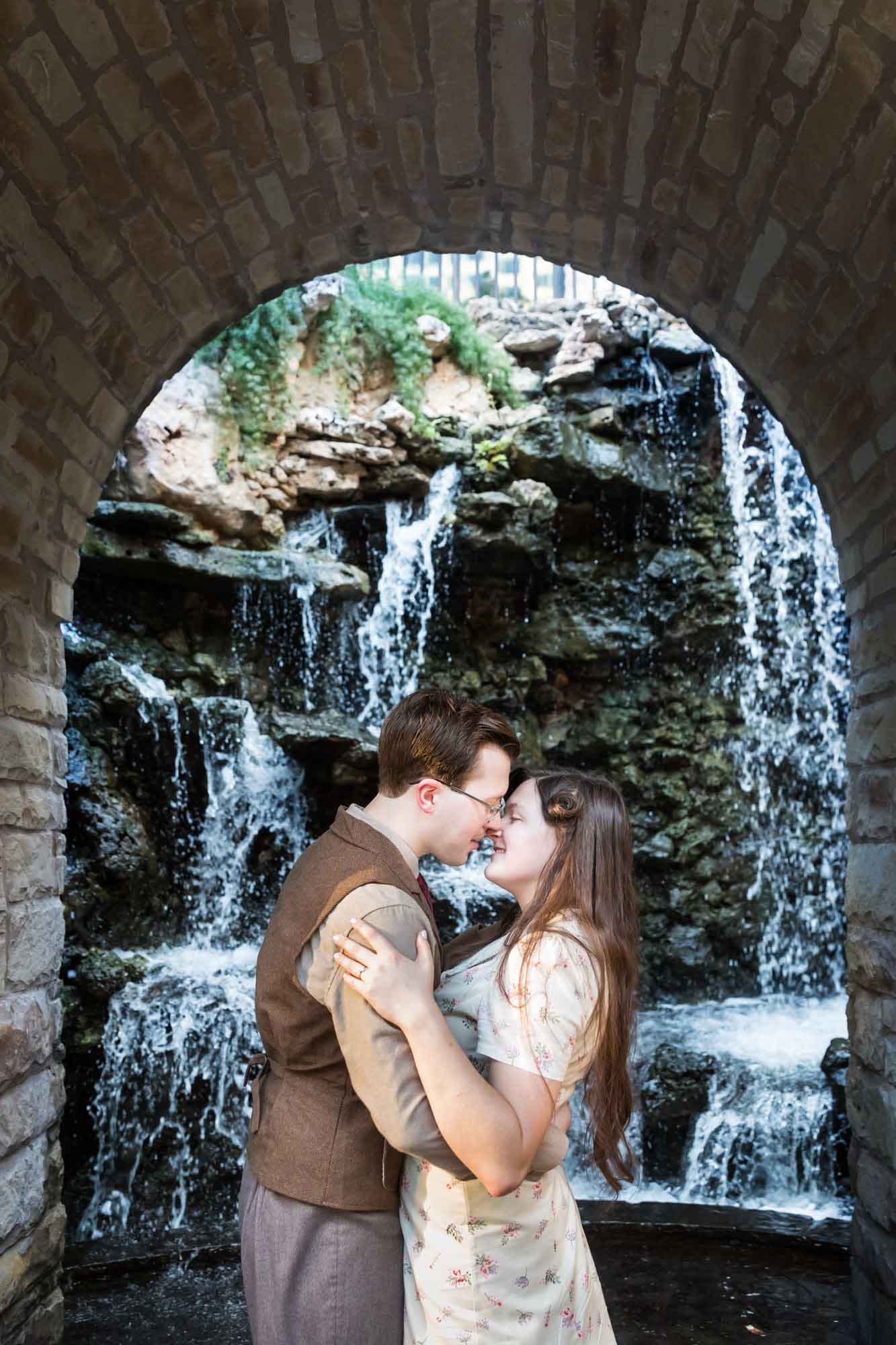 Couple kissing in front of archway in front of waterfall during a River Walk surprise proposal