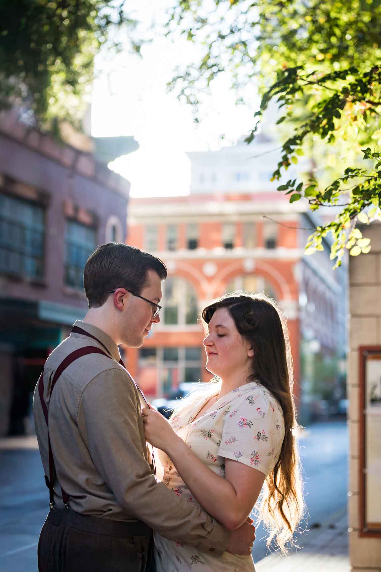 Woman adjusting man's suspenders in the street while wearing retro outfits from the 1940s during a River Walk surprise proposal