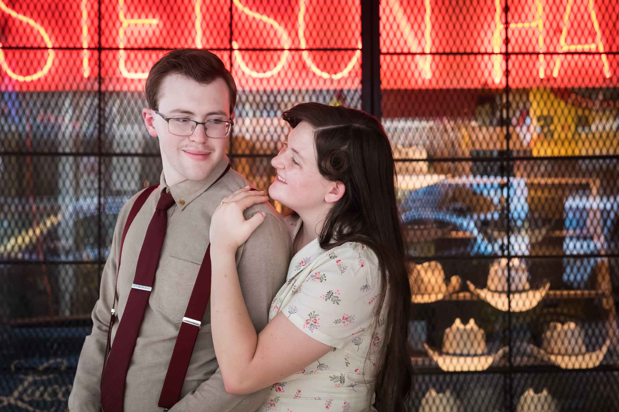 Woman hugging man from behind in front of orange neon sign that says 'Stetson Hats' with cowboy hats in window during a River Walk surprise proposal