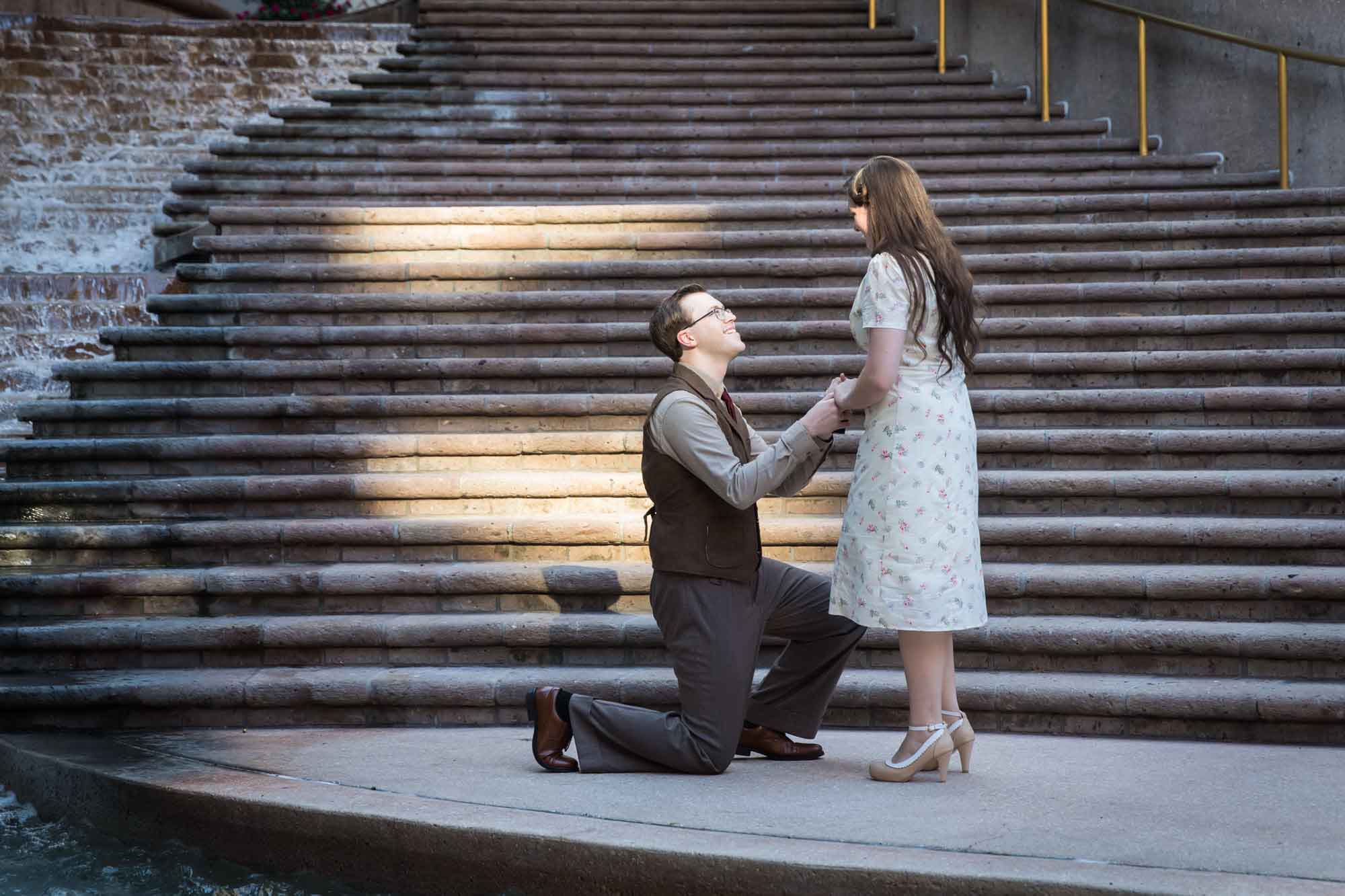 Man down on bended knee proposing to girlfriend on the Weston Centre stairs during a River Walk surprise proposal