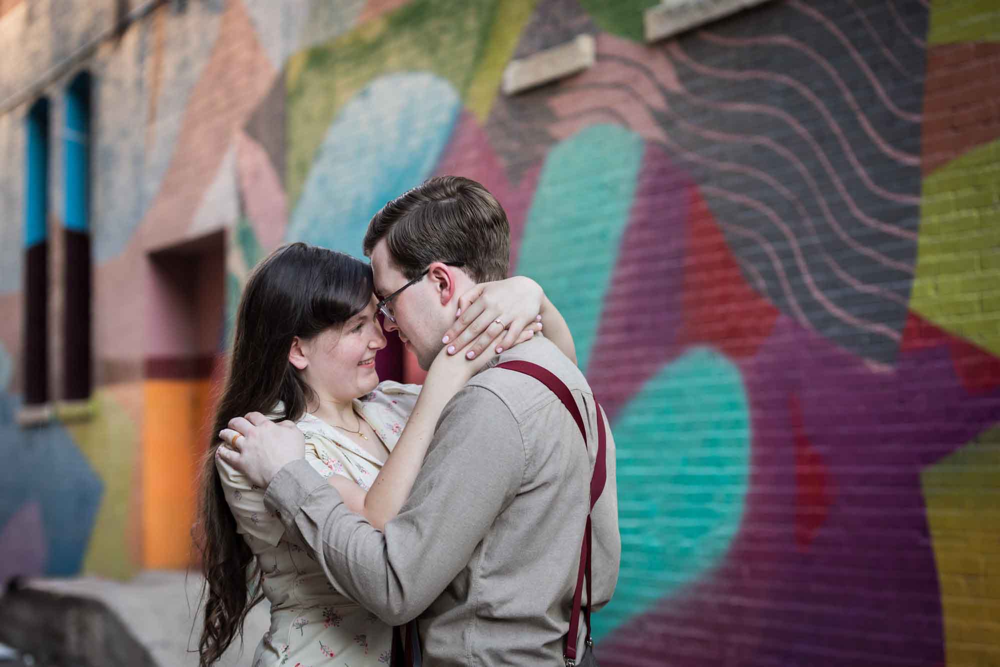Couple wearing retro clothes from the 1940s hugging in front of colored wall murals of Peacock Alley during a River Walk surprise proposal