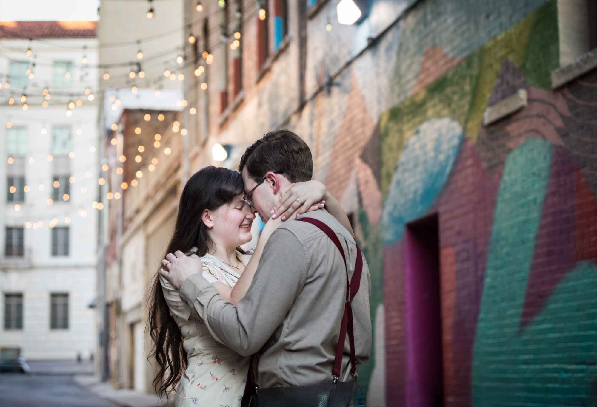 Couple wearing retro clothes from the 1940s hugging in front of colored wall murals of Peacock Alley during a River Walk surprise proposal