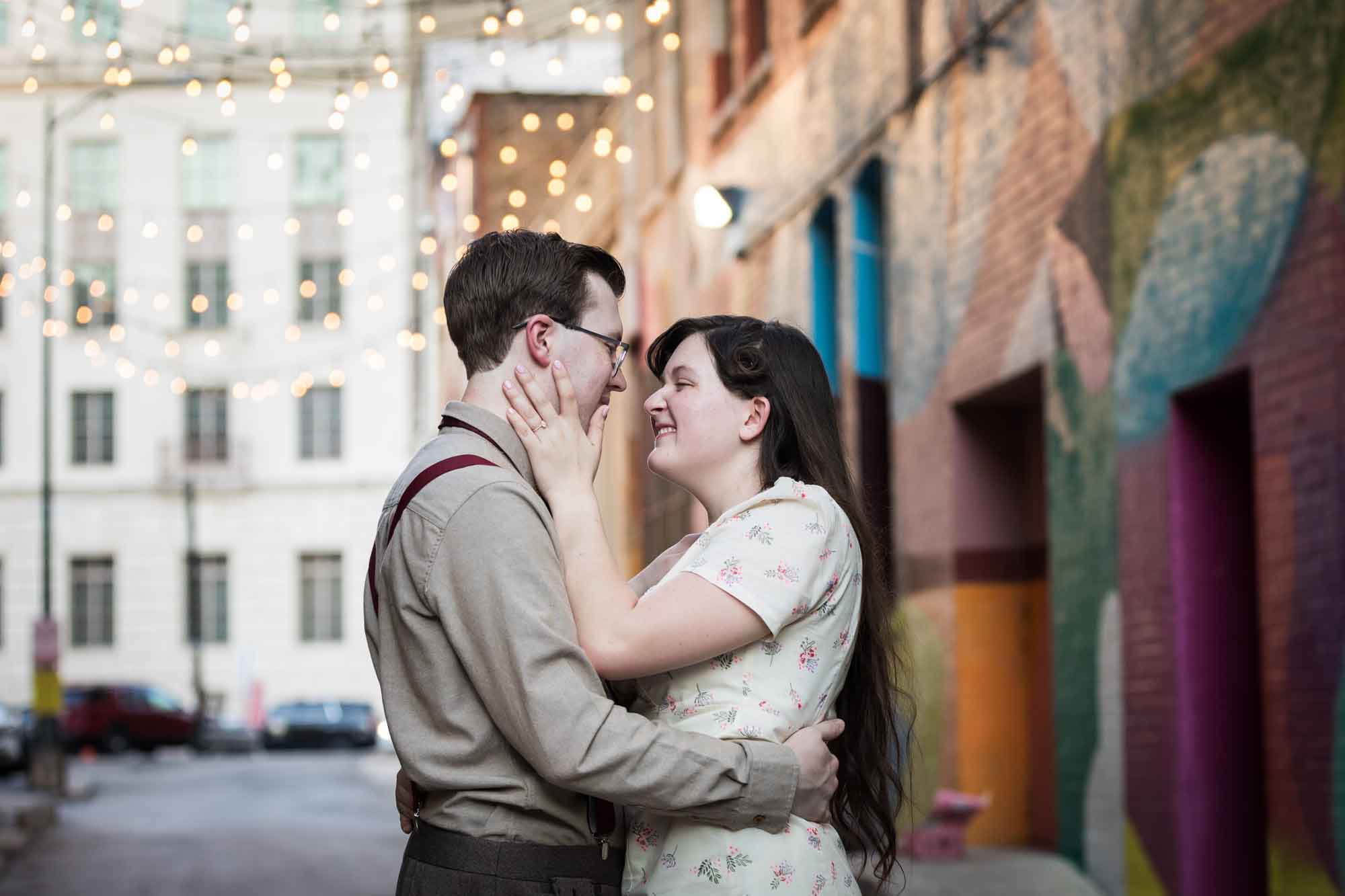 Couple wearing retro clothes from the 1940s hugging in front of colored wall murals of Peacock Alley during a River Walk surprise proposal