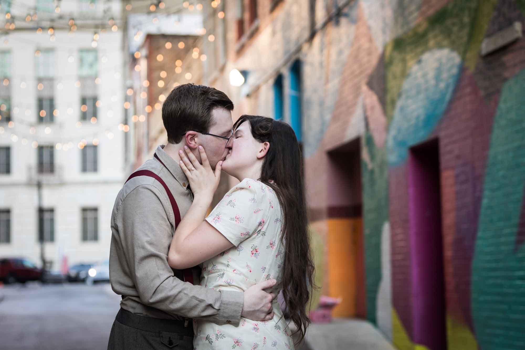 Couple wearing retro clothes from the 1940s kissing in front of colored wall murals of Peacock Alley during a River Walk surprise proposal