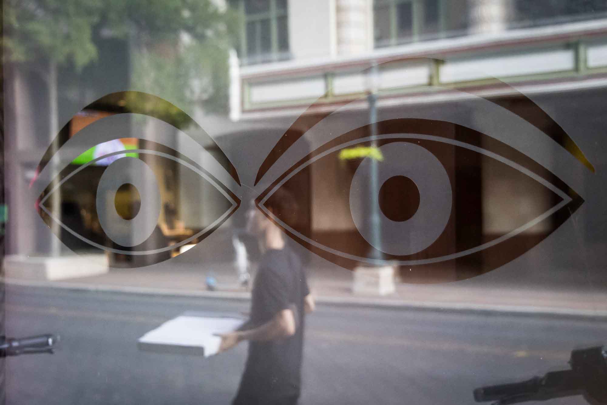 Window with giant eyes and reflection of man walking past in downtown San Antonio