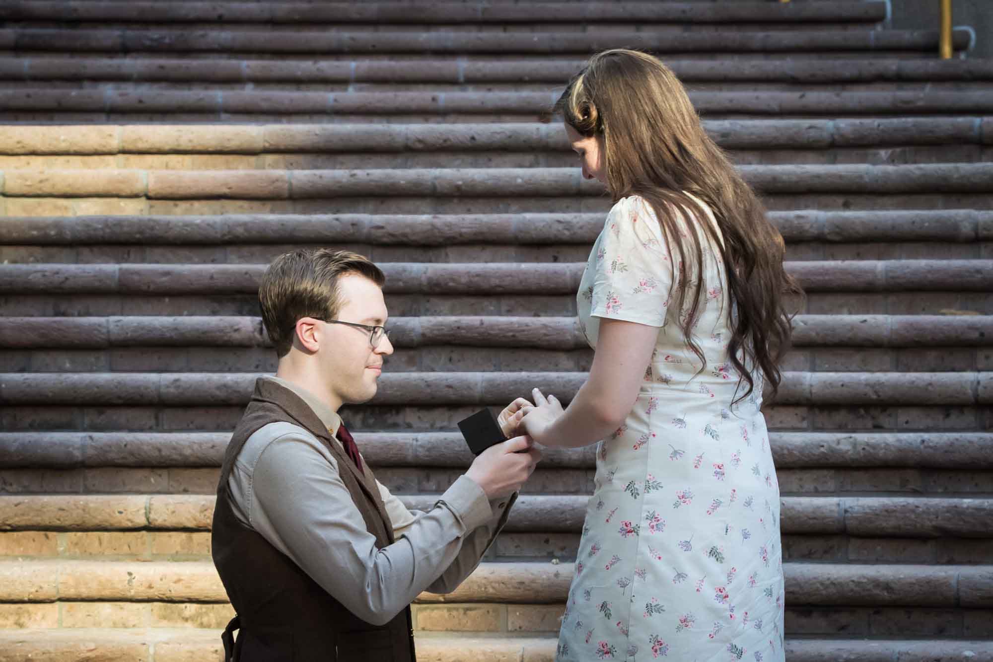 Man down on bended knee putting engagement ring on woman's finger on the Weston Centre stairs during a River Walk surprise proposal