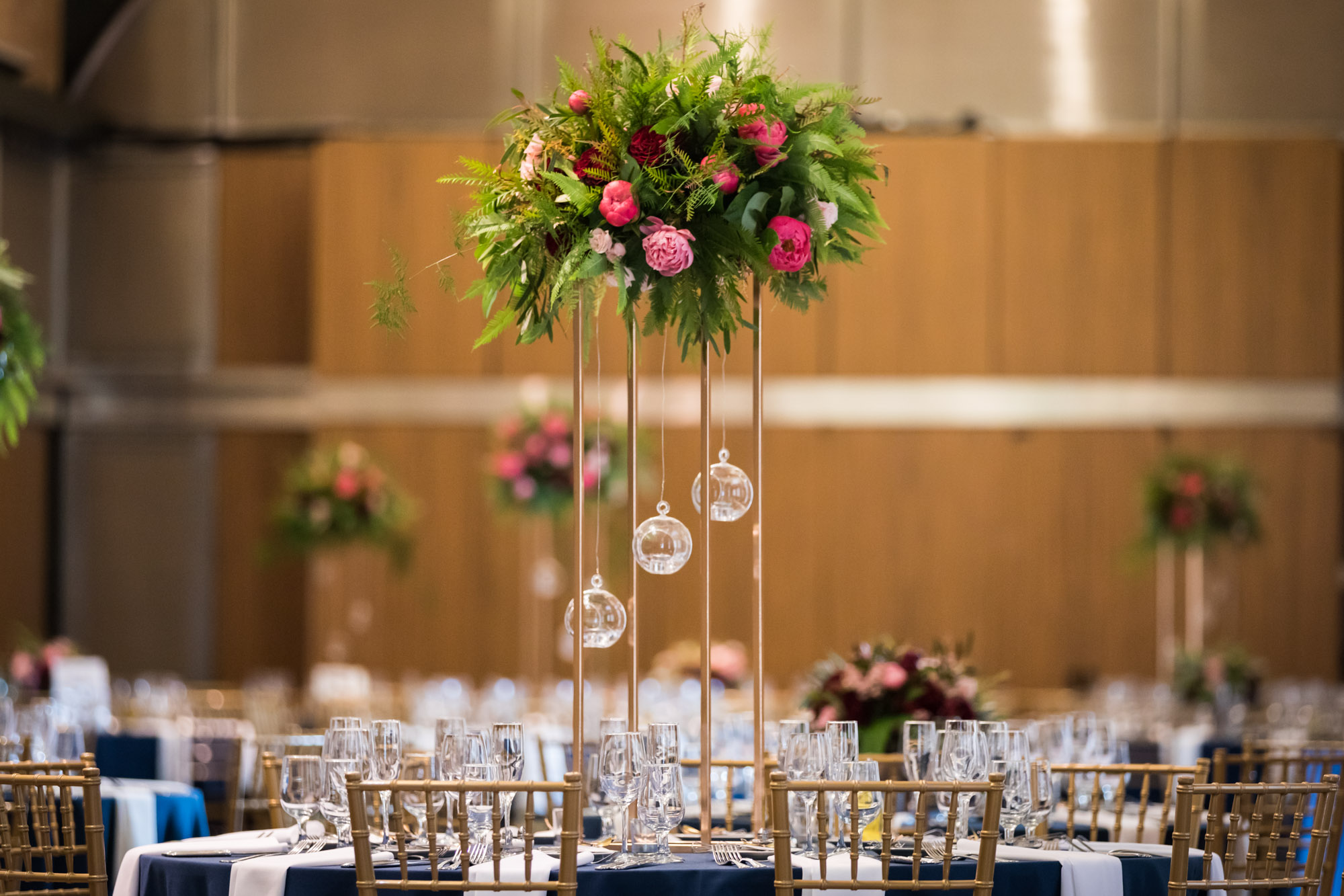 Tables at a wedding reception set with tall centerpieces with ferns and pink peonies and hanging clear balls for an article on unexpected wedding photo tips