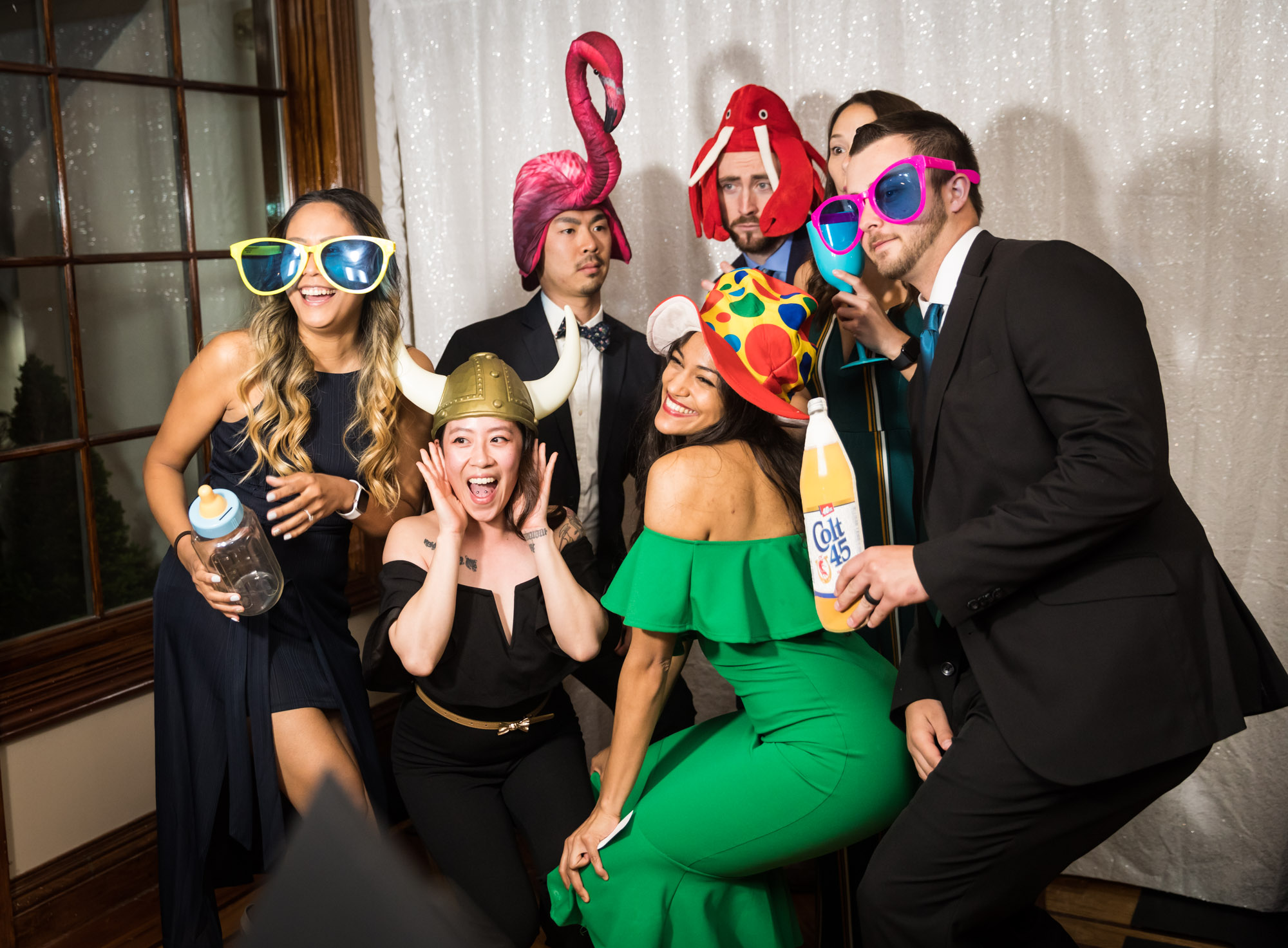 Seven wedding guests wearing wacky hats and sunglasses at a photo booth during a reception for an article on unexpected wedding photo tips