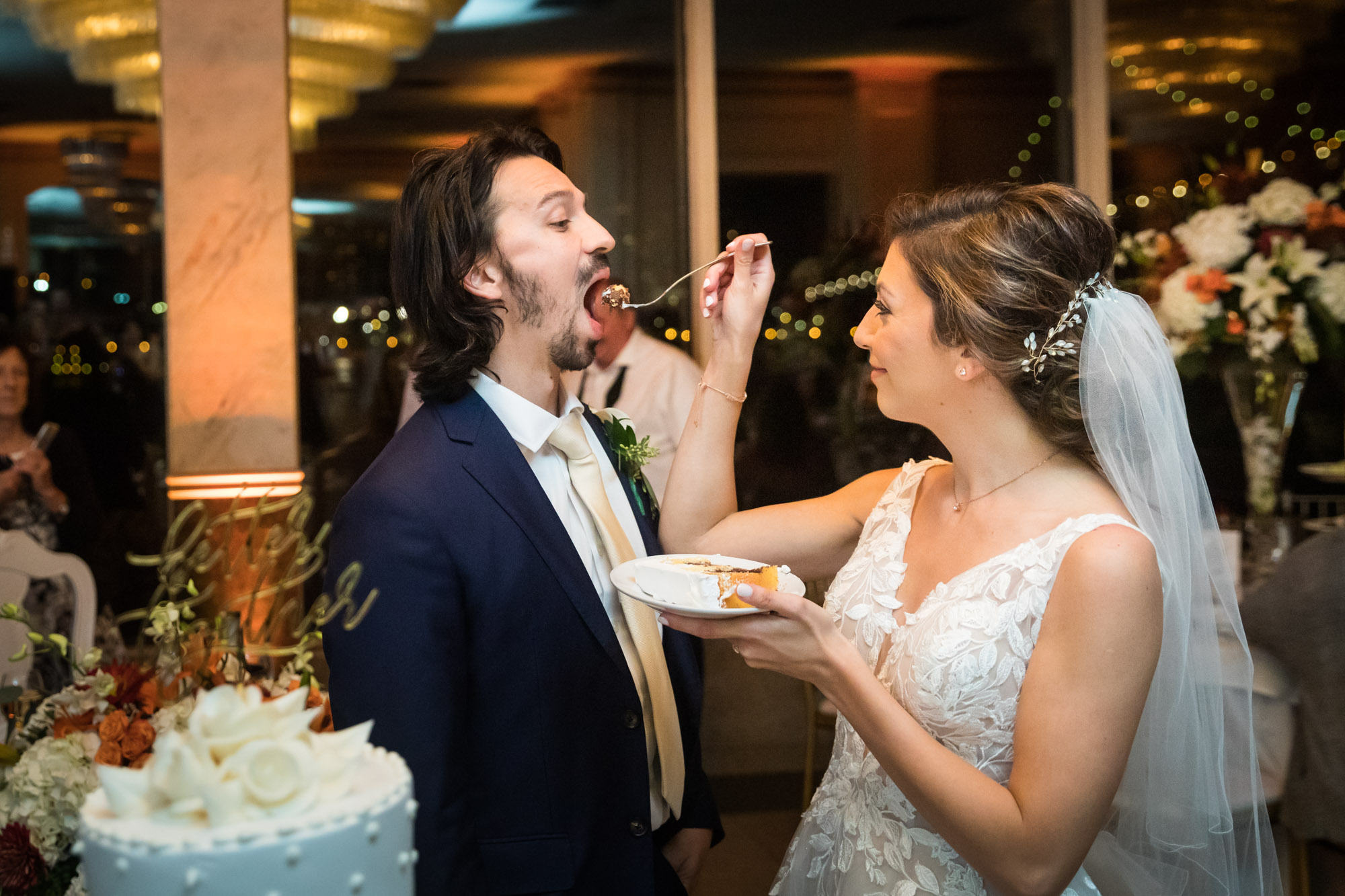 Bride feeding groom with wide open mouth a fork full of cake at reception for an article on unexpected wedding photo tips