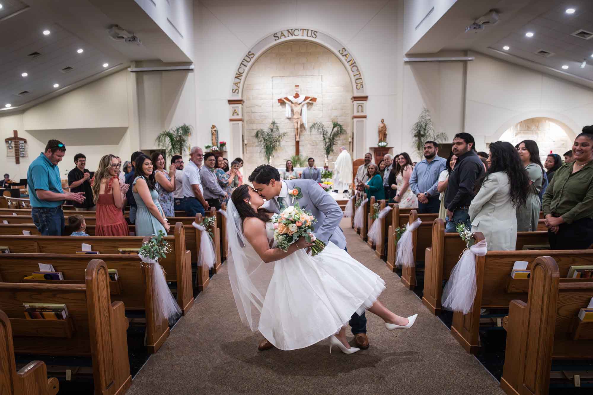 Bride and groom kissing with dip in front of guests in aisle in church after ceremony for an article on unexpected wedding photo tips