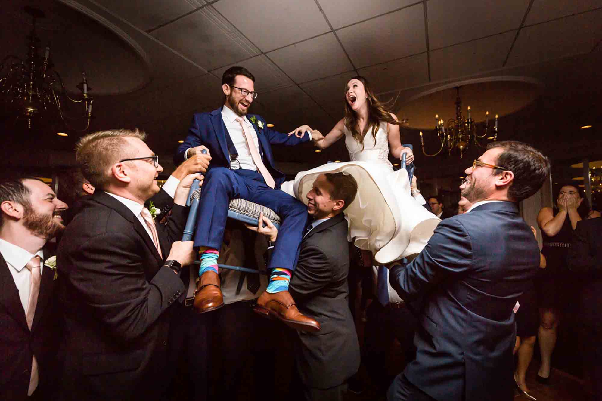 Bride and groom on chairs during hora dance at wedding with guests during reception for an article on unexpected wedding photo tips
