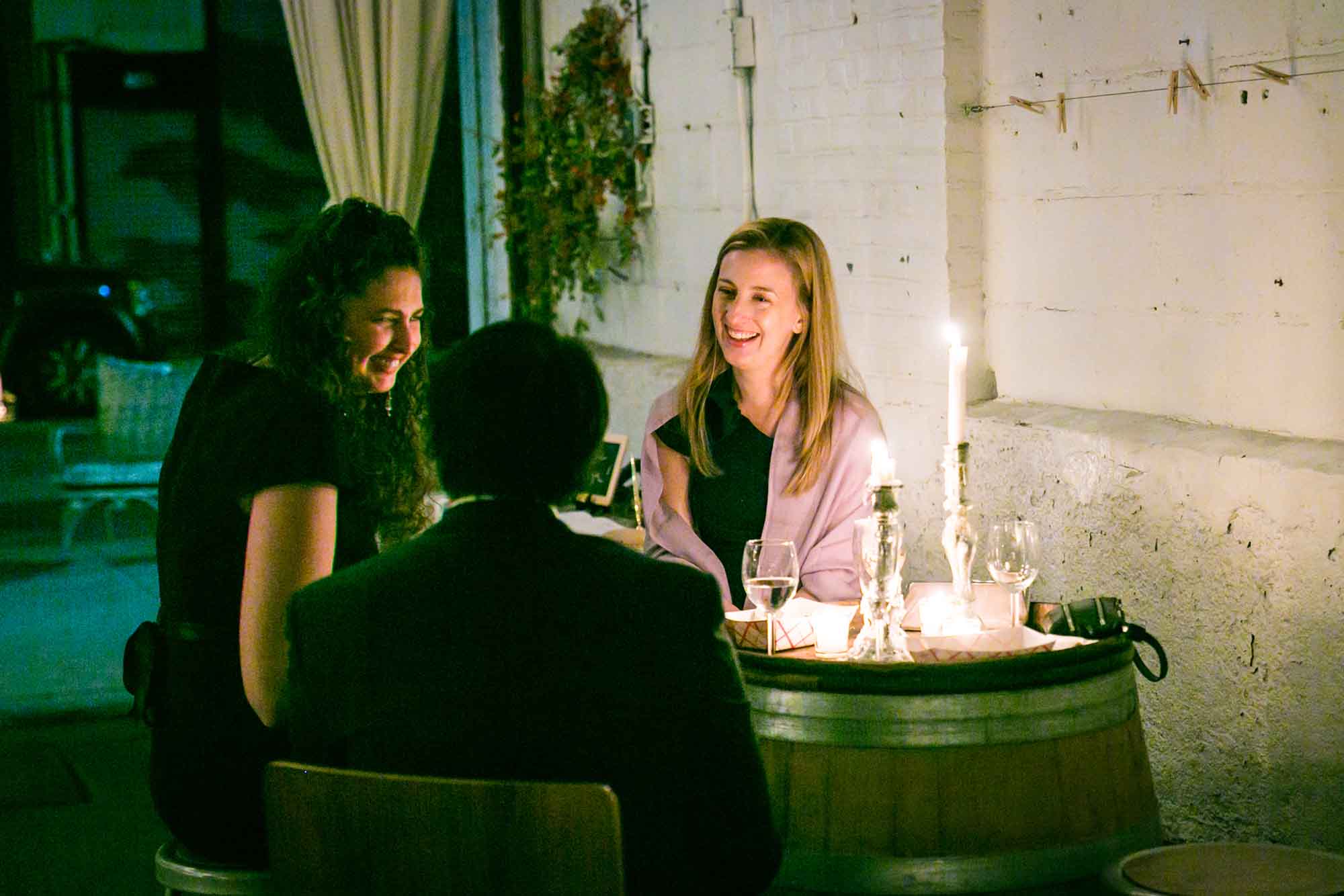 Man and two women talking during wedding reception while seated around table lit with candles for an article on unexpected wedding photo tips