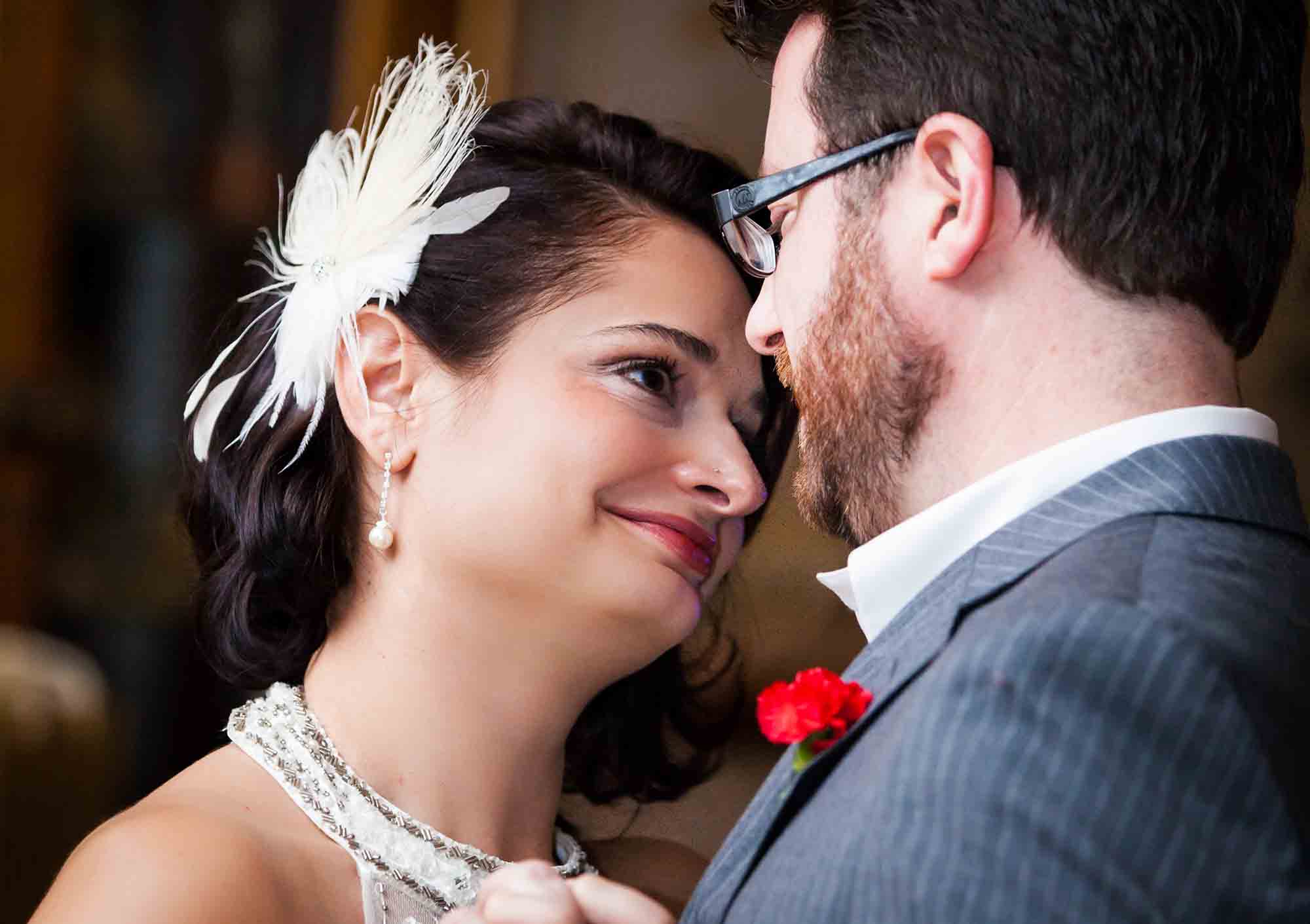 Bride wearing feather headpiece looking at groom wearing glasses while dancing for an article on unexpected wedding photo tips