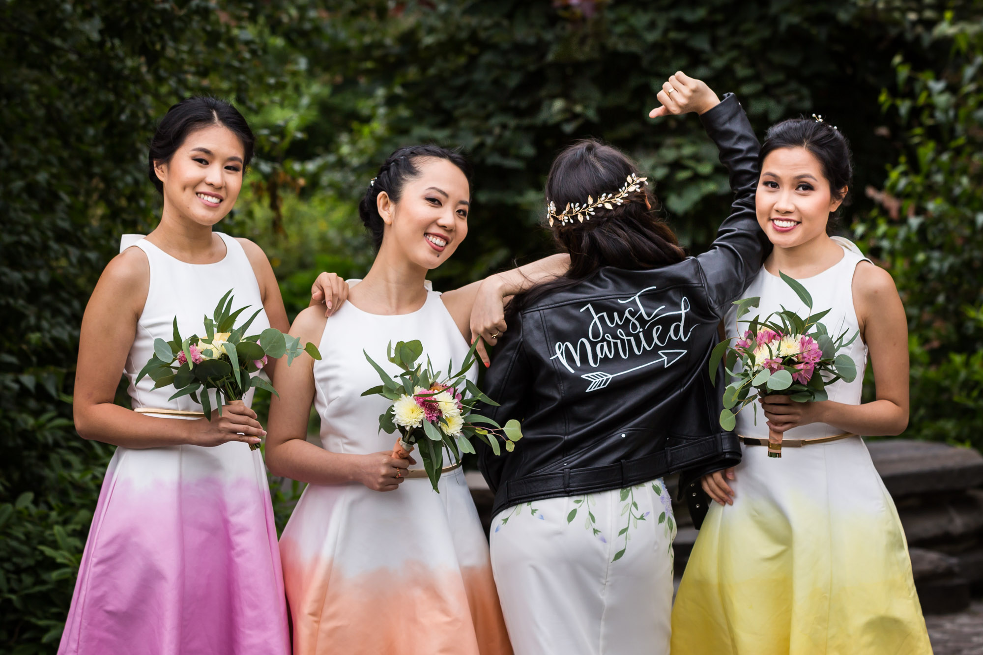 Three bridesmaids posed with bride who is turned around showing off leather jacket saying 'Just Married' on the back for an article on unexpected wedding photo tips