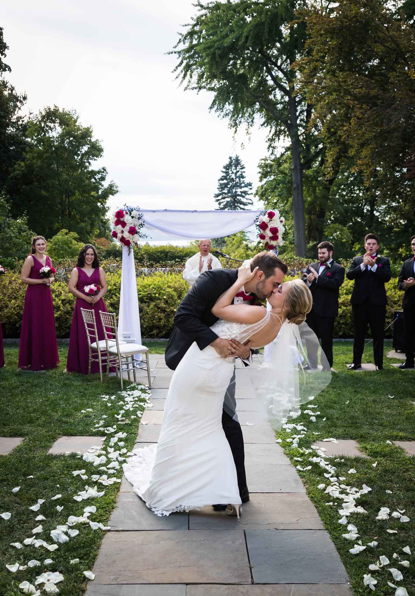 Bride and groom kissing in a dip in front of bridal party in aisle during outdoor wedding for an article on unexpected wedding photo tips