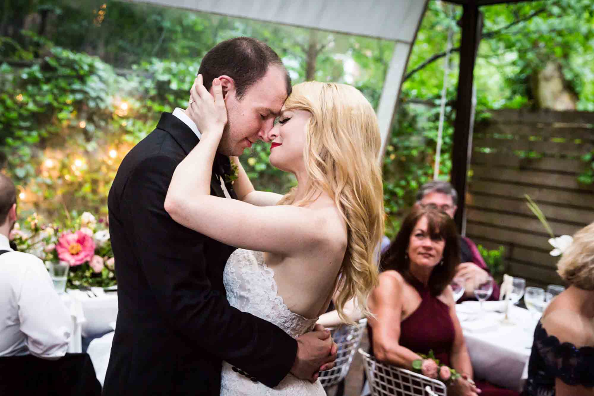Bride holding groom's head while dancing with eyes closed in front of guests for an article on unexpected wedding photo tips