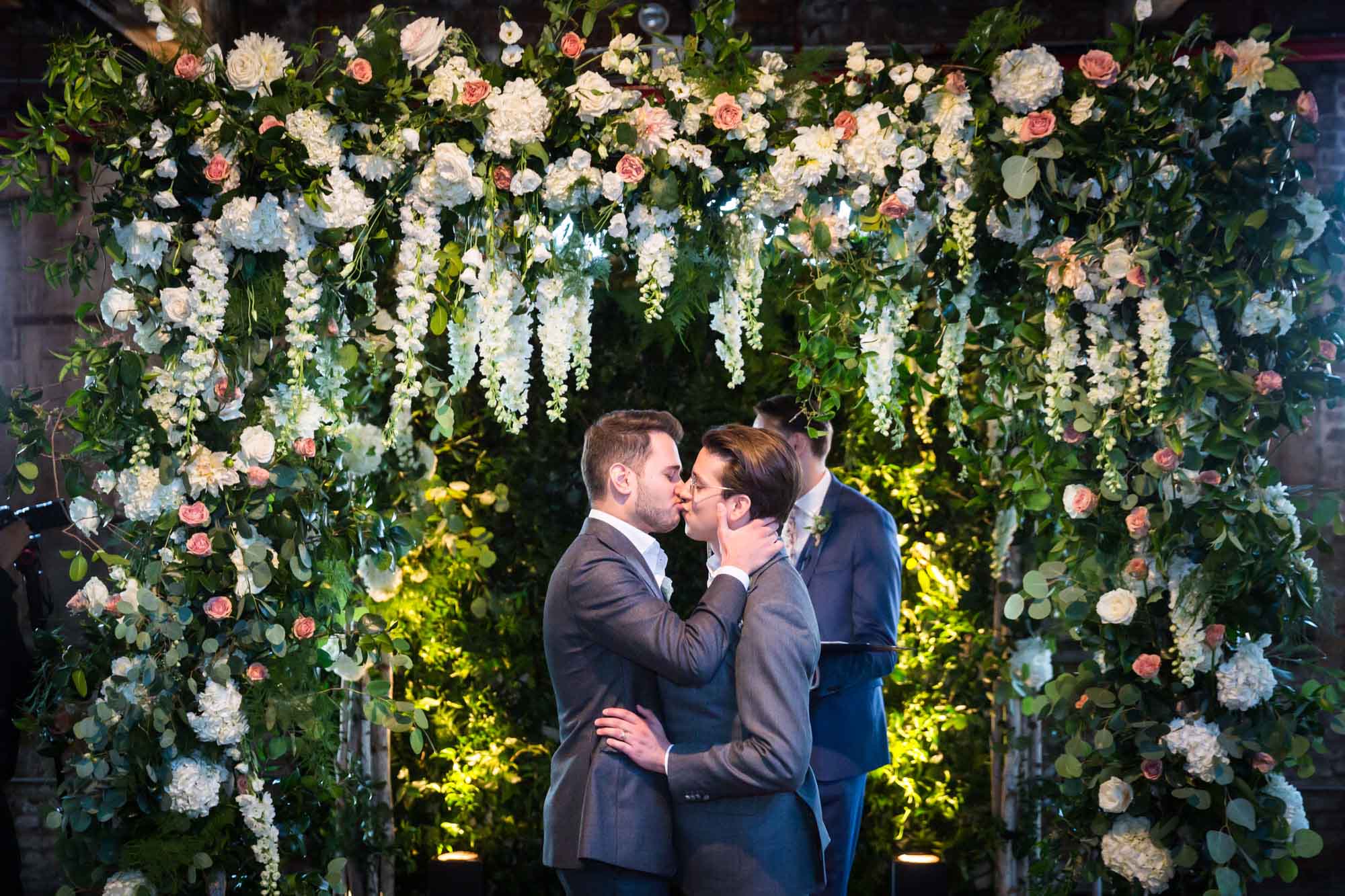Two grooms kissing under large canopy of flowers for an article on unexpected wedding photo tips