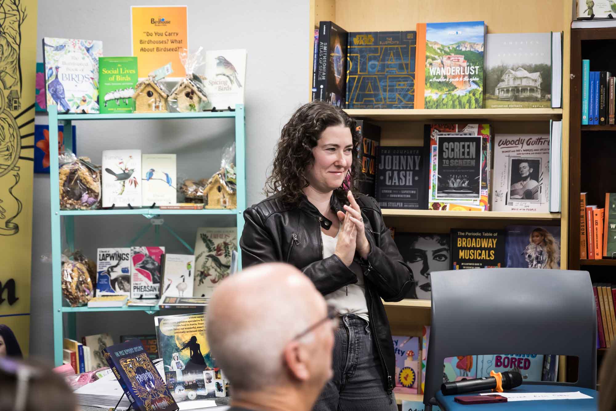 Austin book launch party photos of author Erin Cotter speaking into microphone in front of shelves filled with books