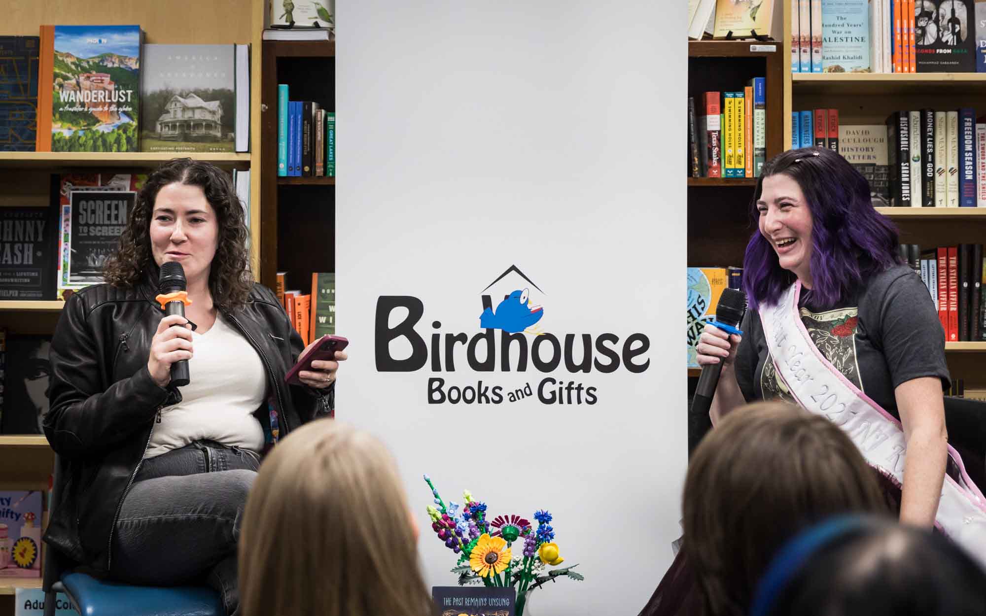 Austin book launch party photos of authors Nancy Knight and Erin Cotter speaking into microphone in front of shelves filled with books